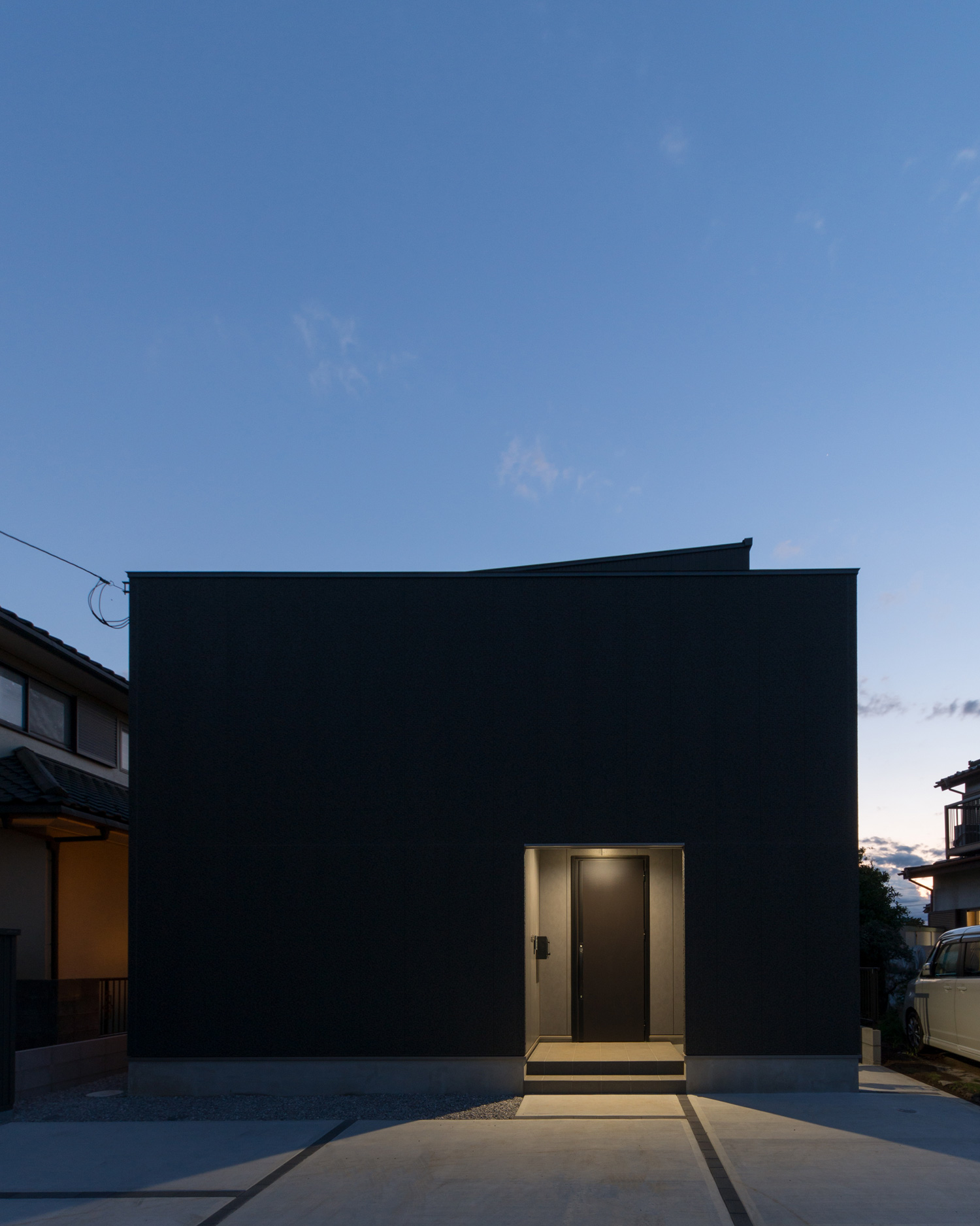 玄関が照明に照らされた黒いキューブ状の外観の住まい・デザイン住宅