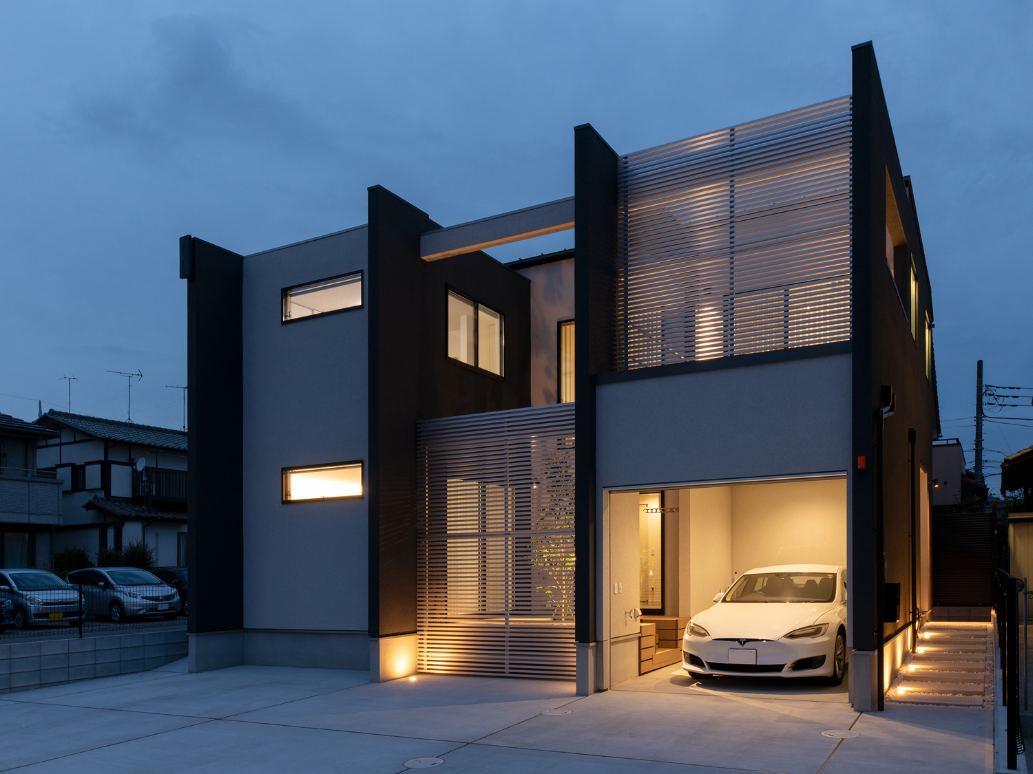 インナーガレージとアプローチが照明に照らされる住宅の外観・デザイン住宅