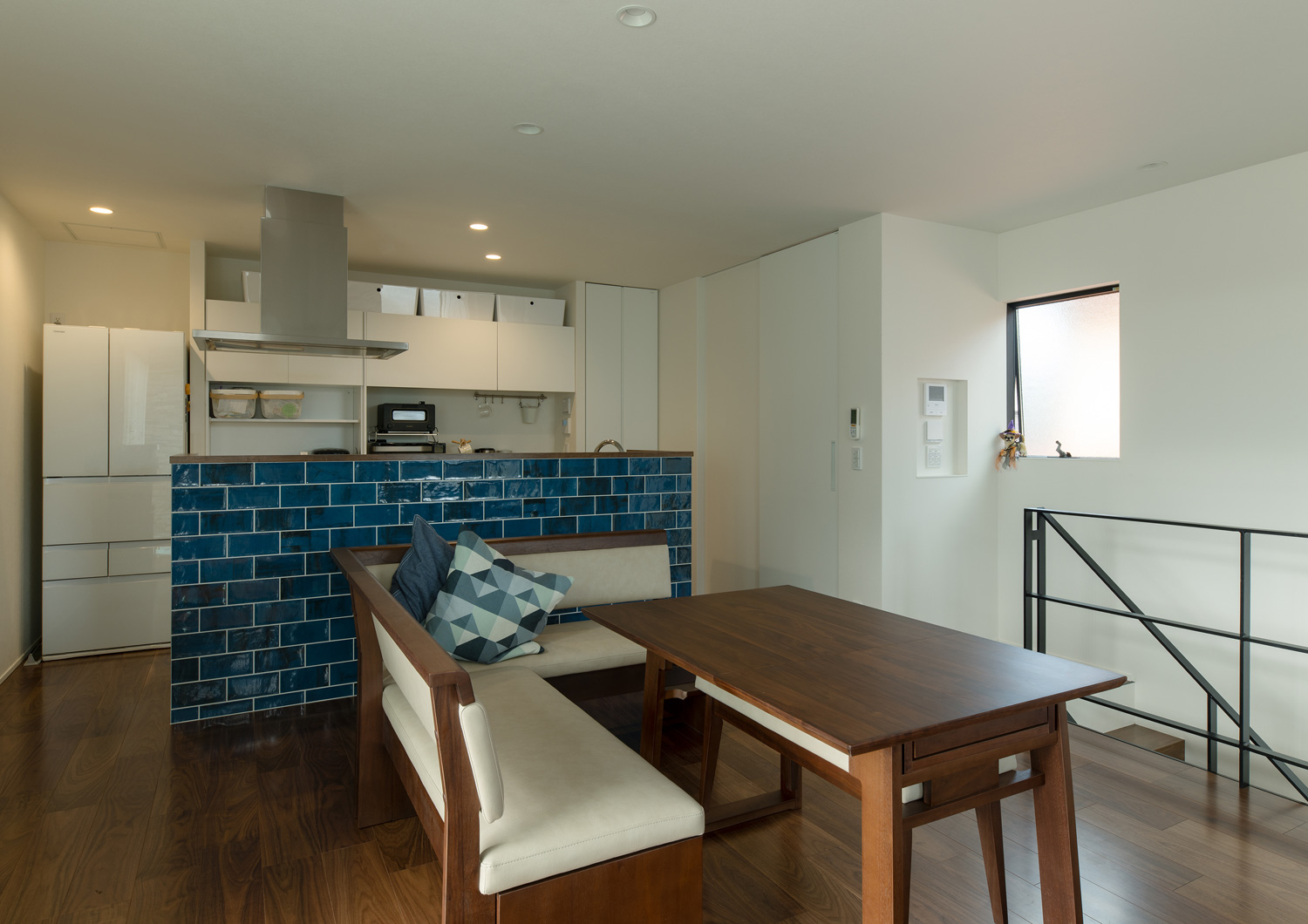 青いタイルの腰壁付きキッチンの前に木製のダイニングテーブルとソファーがあるLDK・デザイン住宅