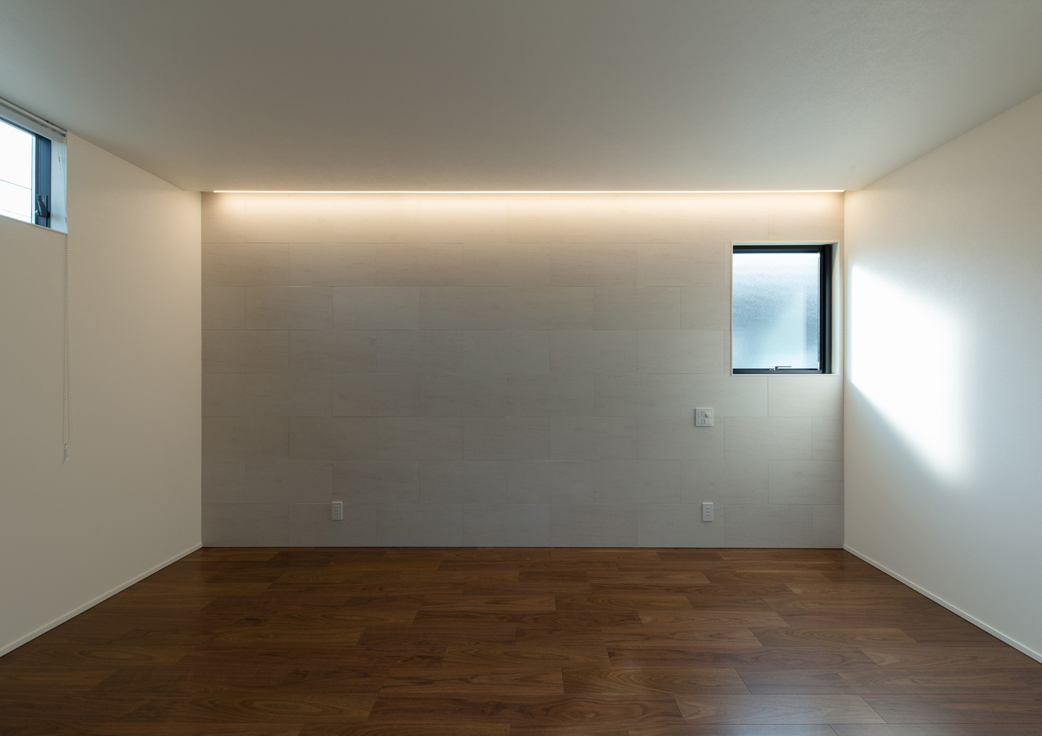 壁際に間接照明を取り付けた、小さい窓のある部屋・デザイン住宅