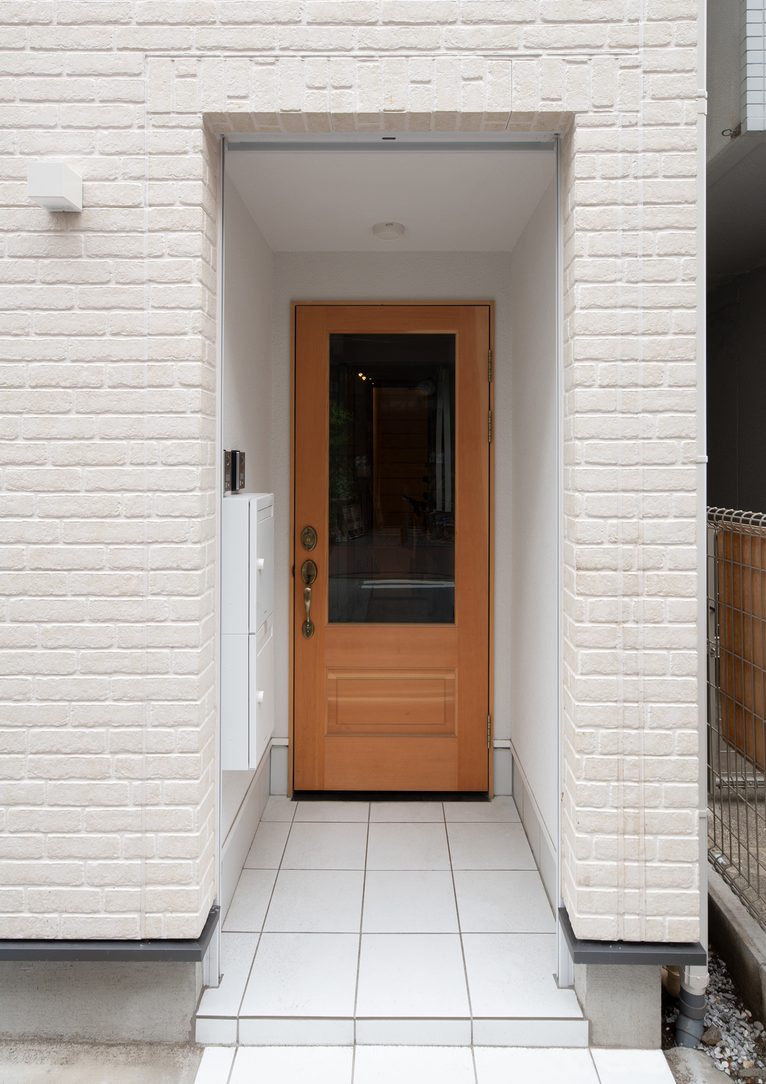 白い外壁の玄関にガラス窓付きの木製の玄関扉がある様子・デザイン住宅