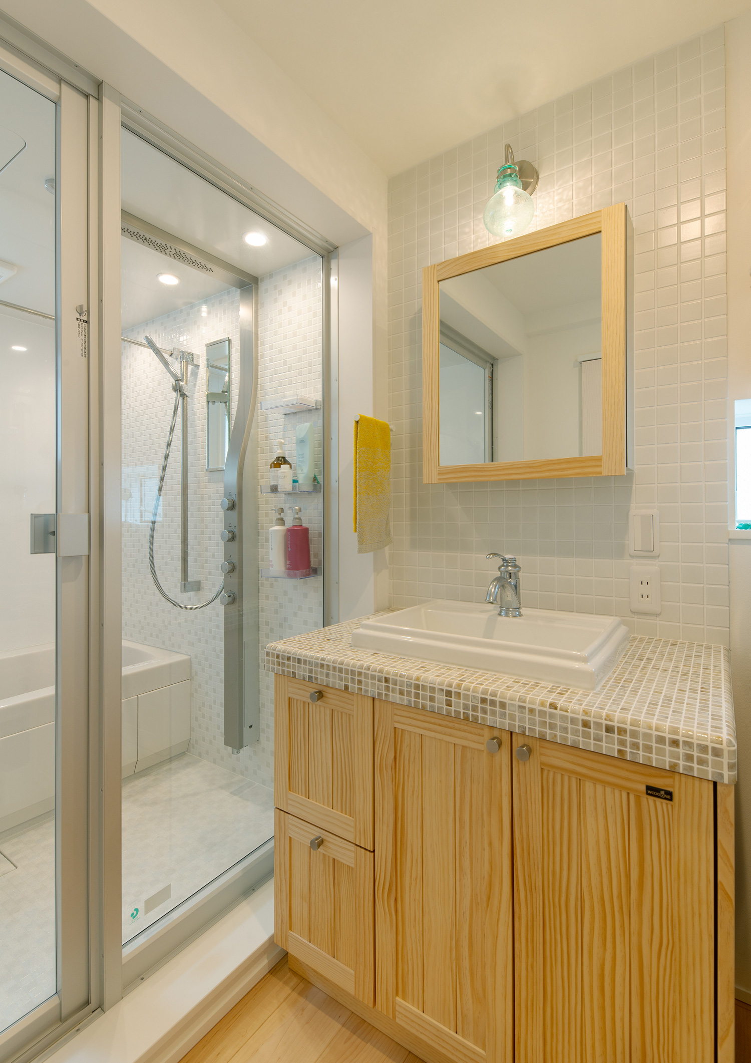 壁や洗面台にタイルを使用した、浴室とガラス扉で繋がった洗面所・デザイン住宅