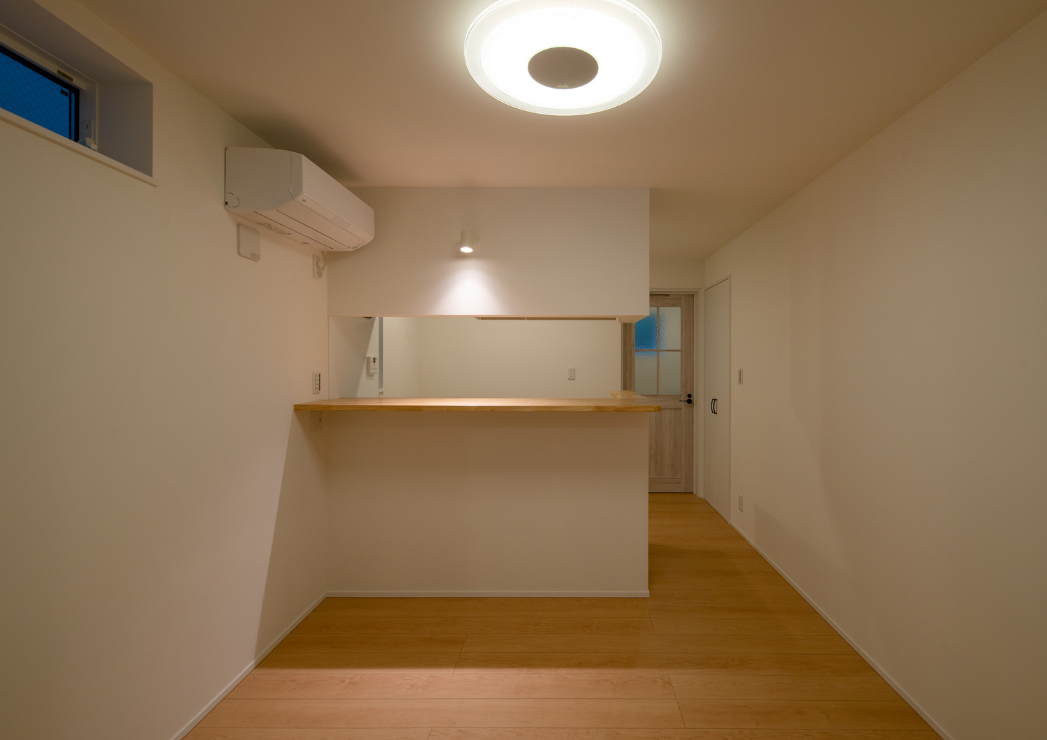 シーリングライトと、キッチンのカウンターを照らすスポットライトが取り付けられたシンプルなワンルーム・デザイン住宅
