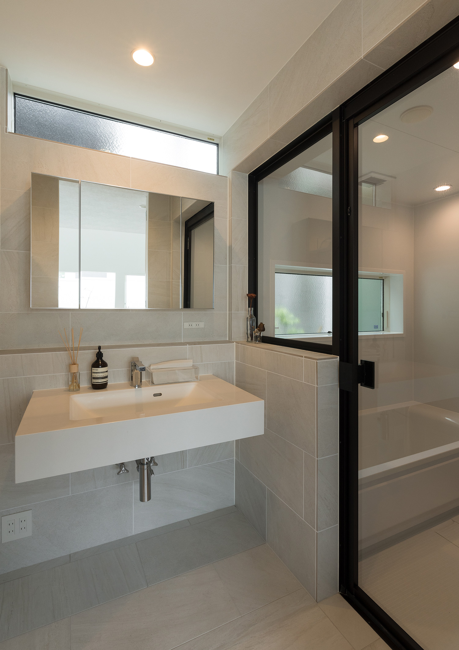 白いタイル壁の洗面所と浴室がガラス扉で仕切られている様子・デザイン住宅