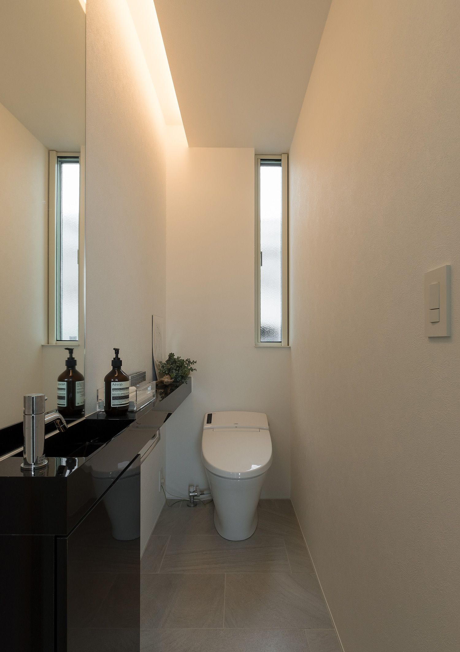 壁際に間接照明を取り付けた黒い薄型手洗いのあるトイレ・デザイン住宅
