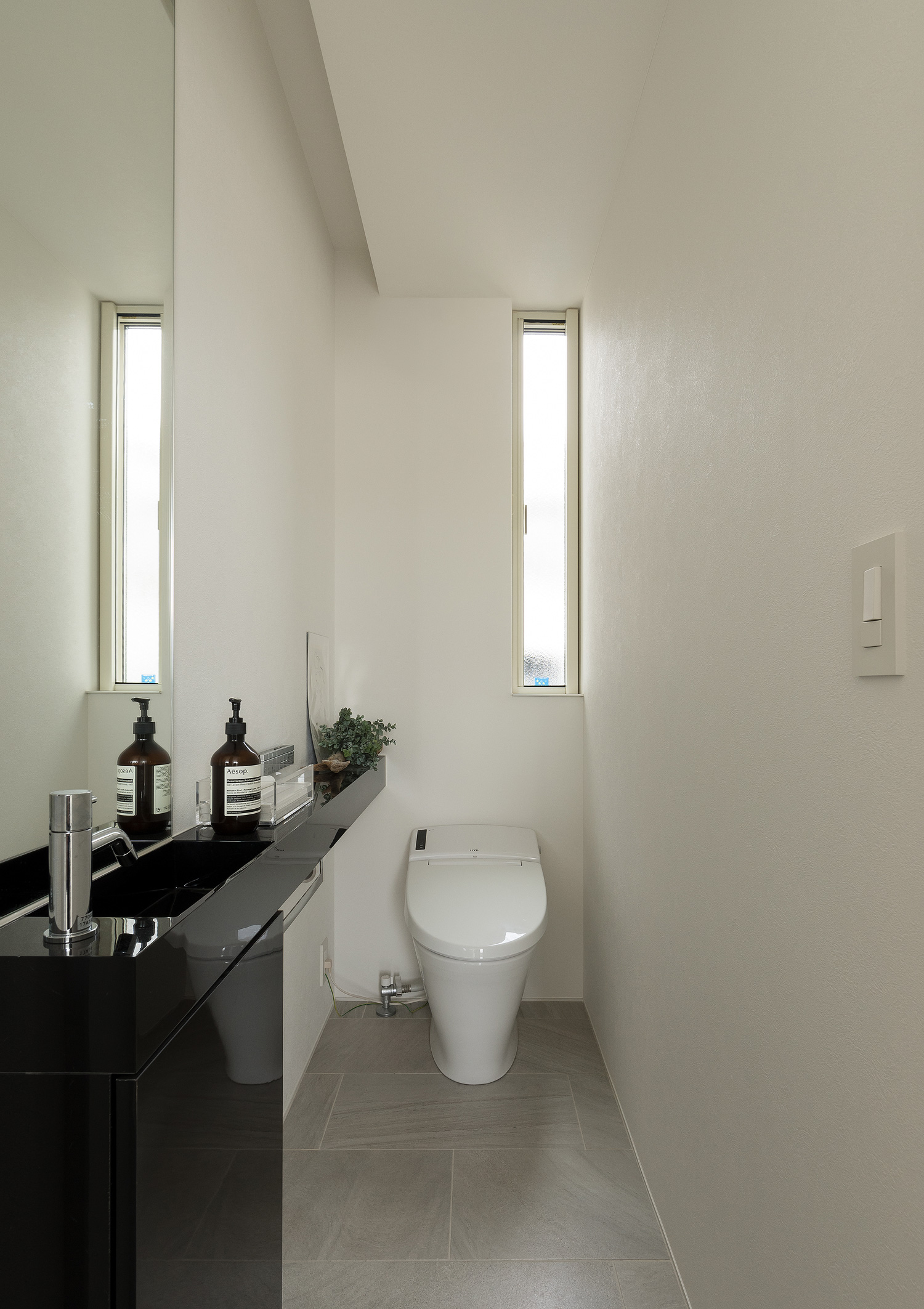縦長のスリット窓が取り付けられた、黒い薄型手洗いのあるトイレ・デザイン住宅