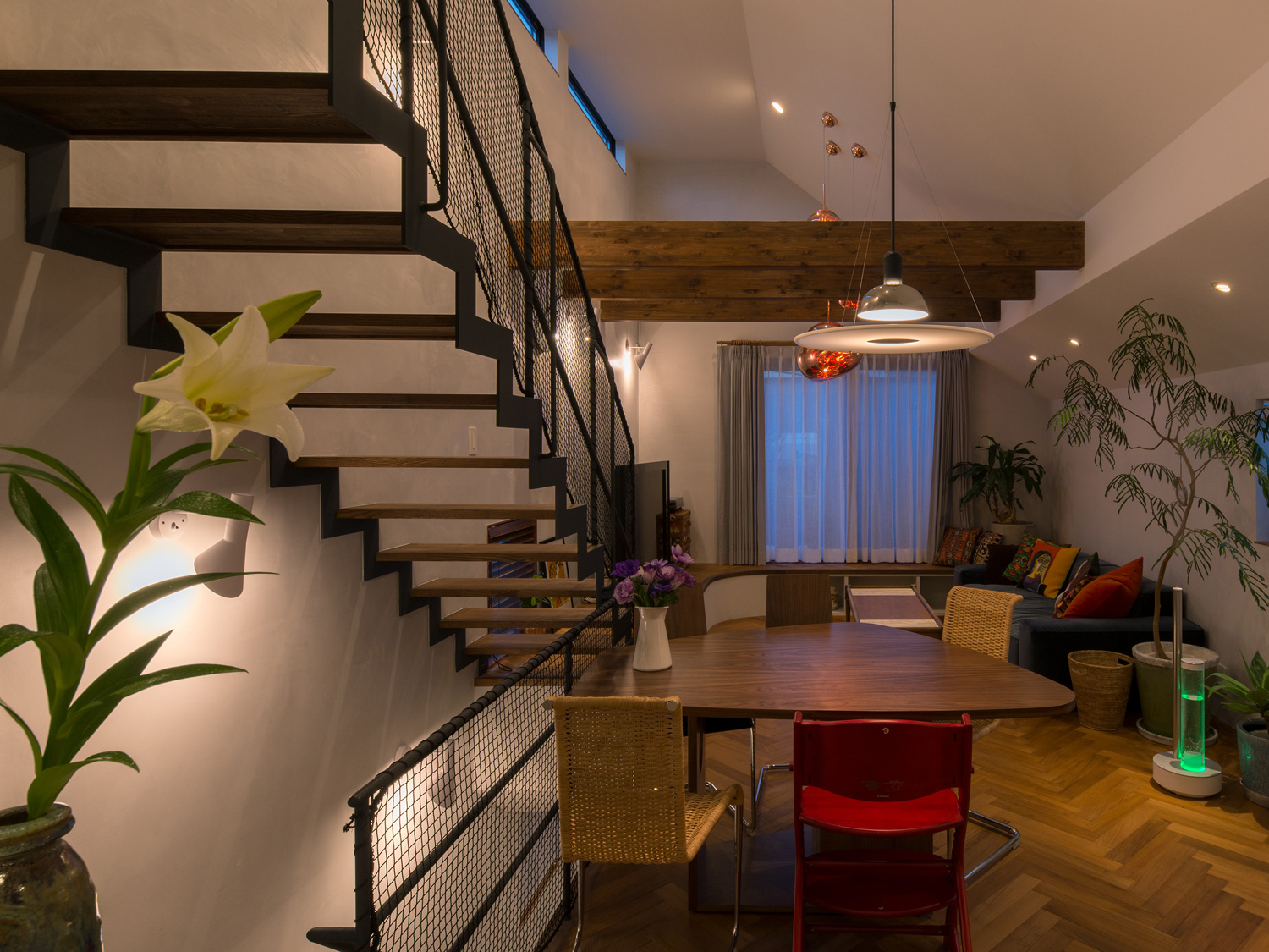 壁に取り付けられたスポットライトやペンダントに照らされるヘリンボーン柄の床のLDK・デザイン住宅