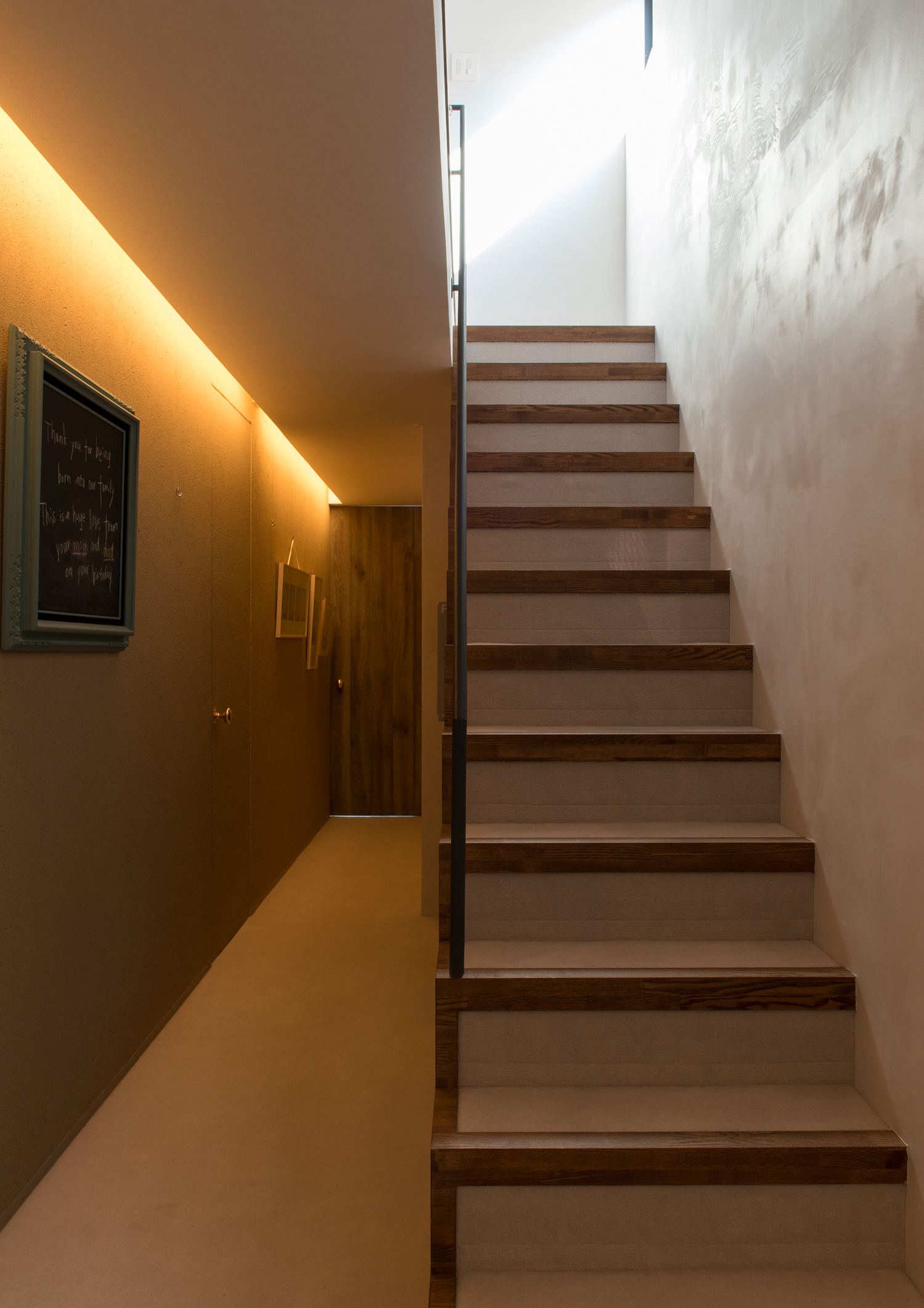 壁際に照明が取り付けられた廊下の横にある階段・デザイン住宅