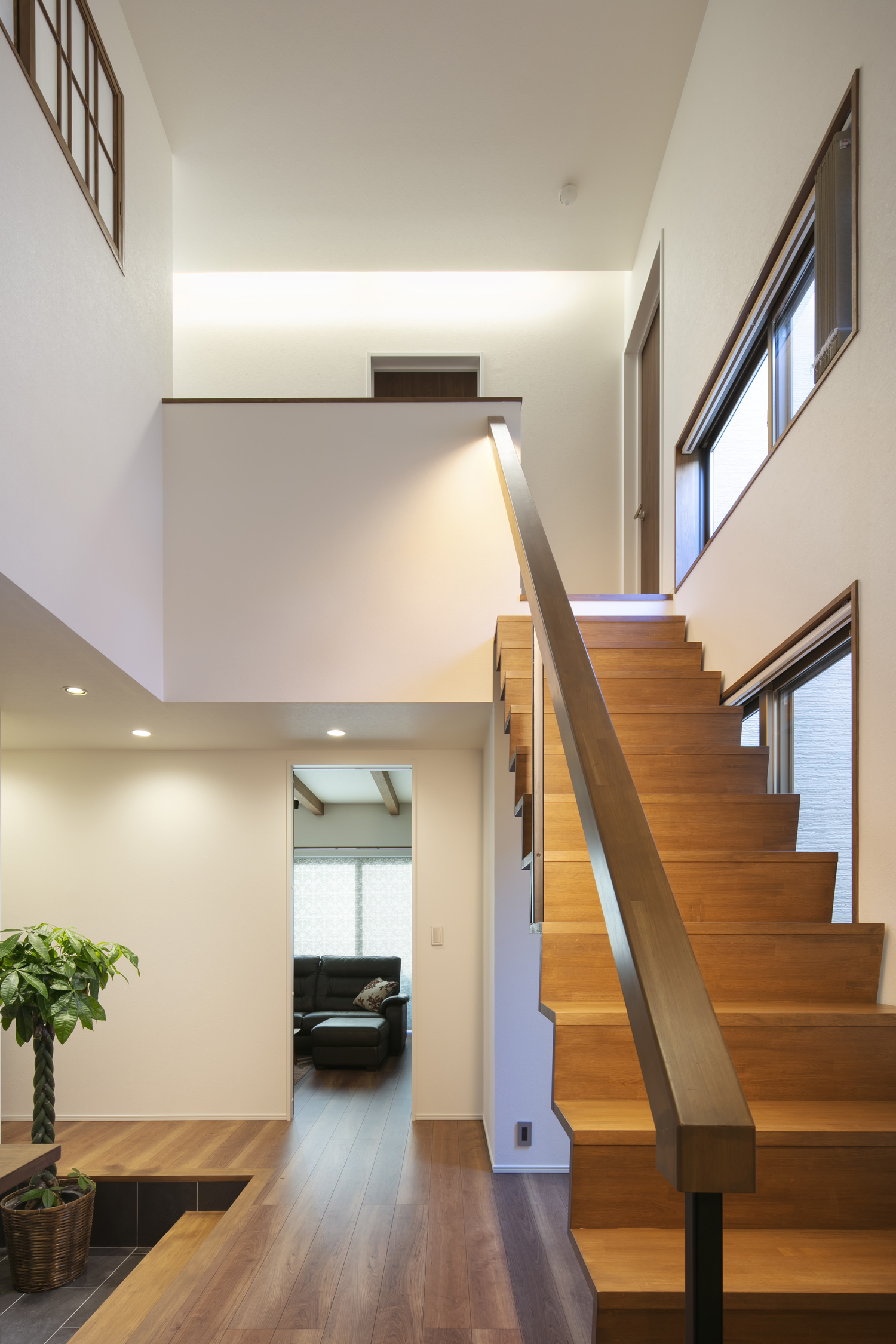 二階の天井の間接照明に照らされた、吹き抜けにある木製のスケルトン階段・デザイン住宅