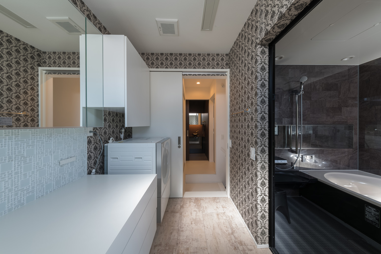 浴室とダマスク柄の壁紙の洗面所が隣接した空間・デザイン住宅