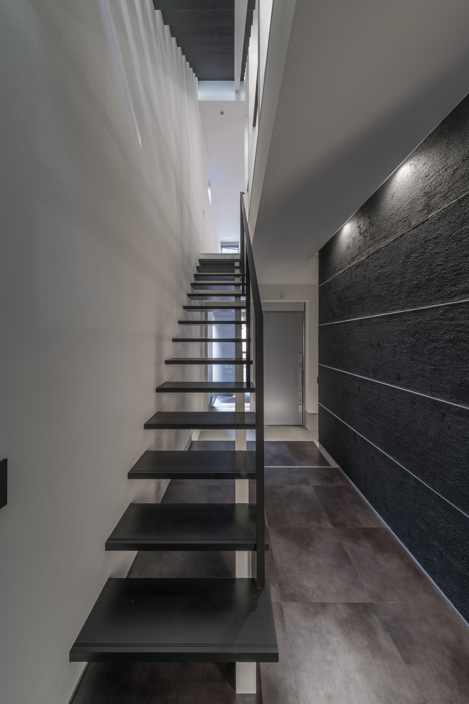玄関の上を横切るように設けられた黒いスケルトン階段・デザイン住宅