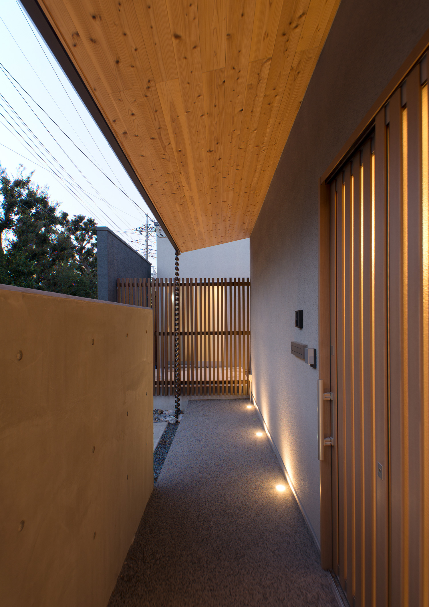 地面に間接照明が取り付けられた、木目の庇がある玄関アプローチ・デザイン住宅