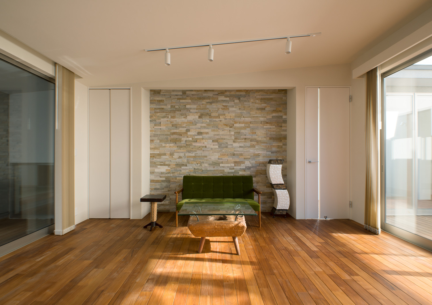 タイルのアクセントウォールの前に緑色のソファーやガラスのサイドテーブルを置いたフローリングのLDK・デザイン住宅