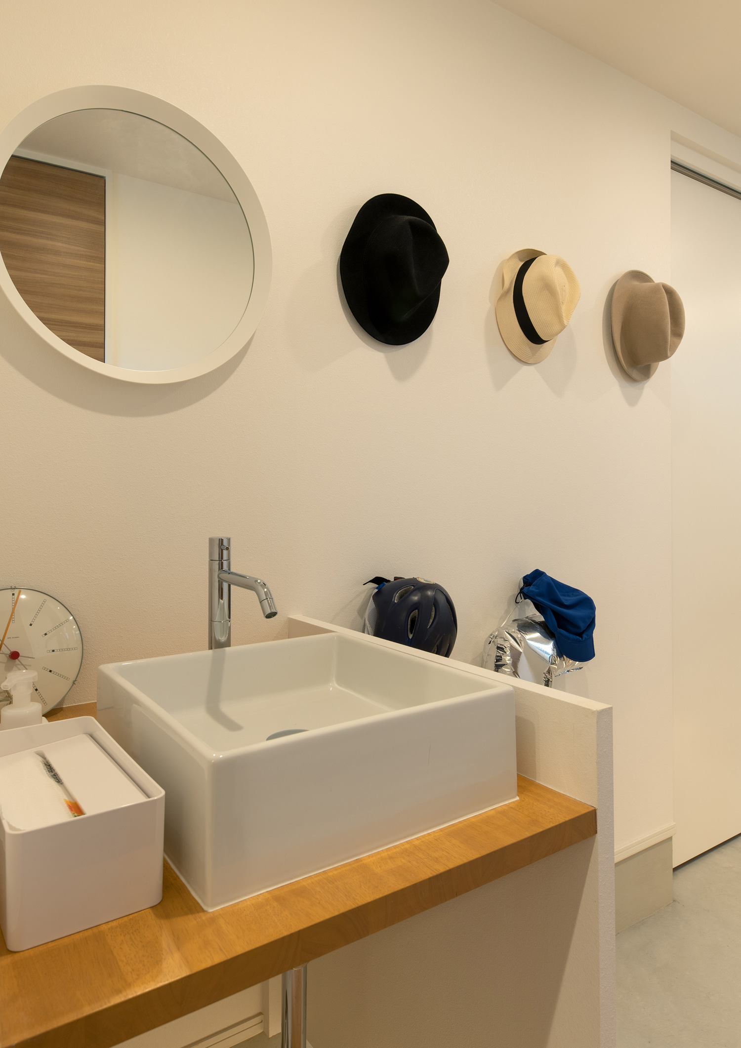丸い鏡のある手洗いカウンターのそばに帽子が飾られた壁がある様子・デザイン住宅