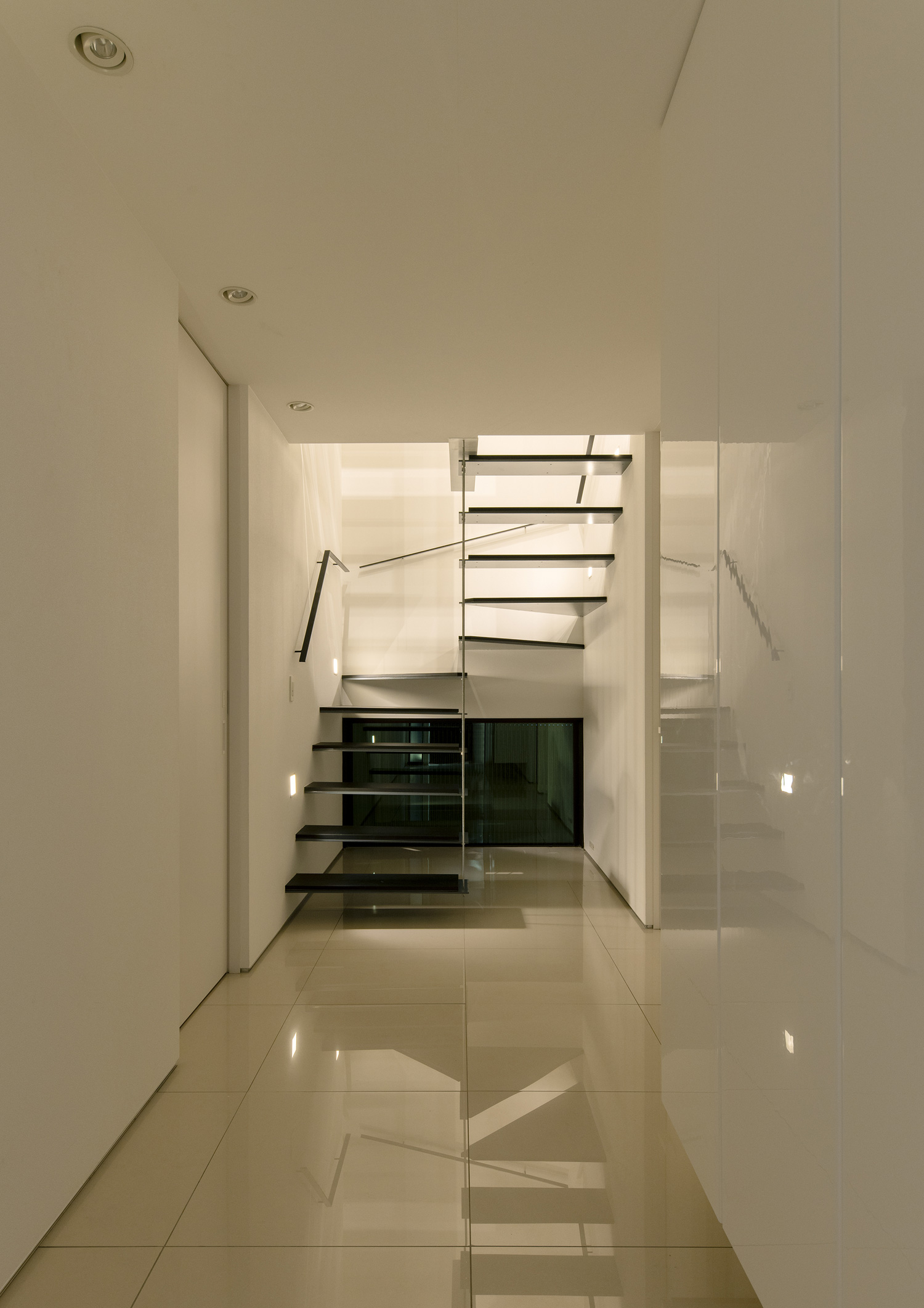 白い壁に埋め込まれた照明により黒いスケルトン階段が照らされる様子・デザイン住宅