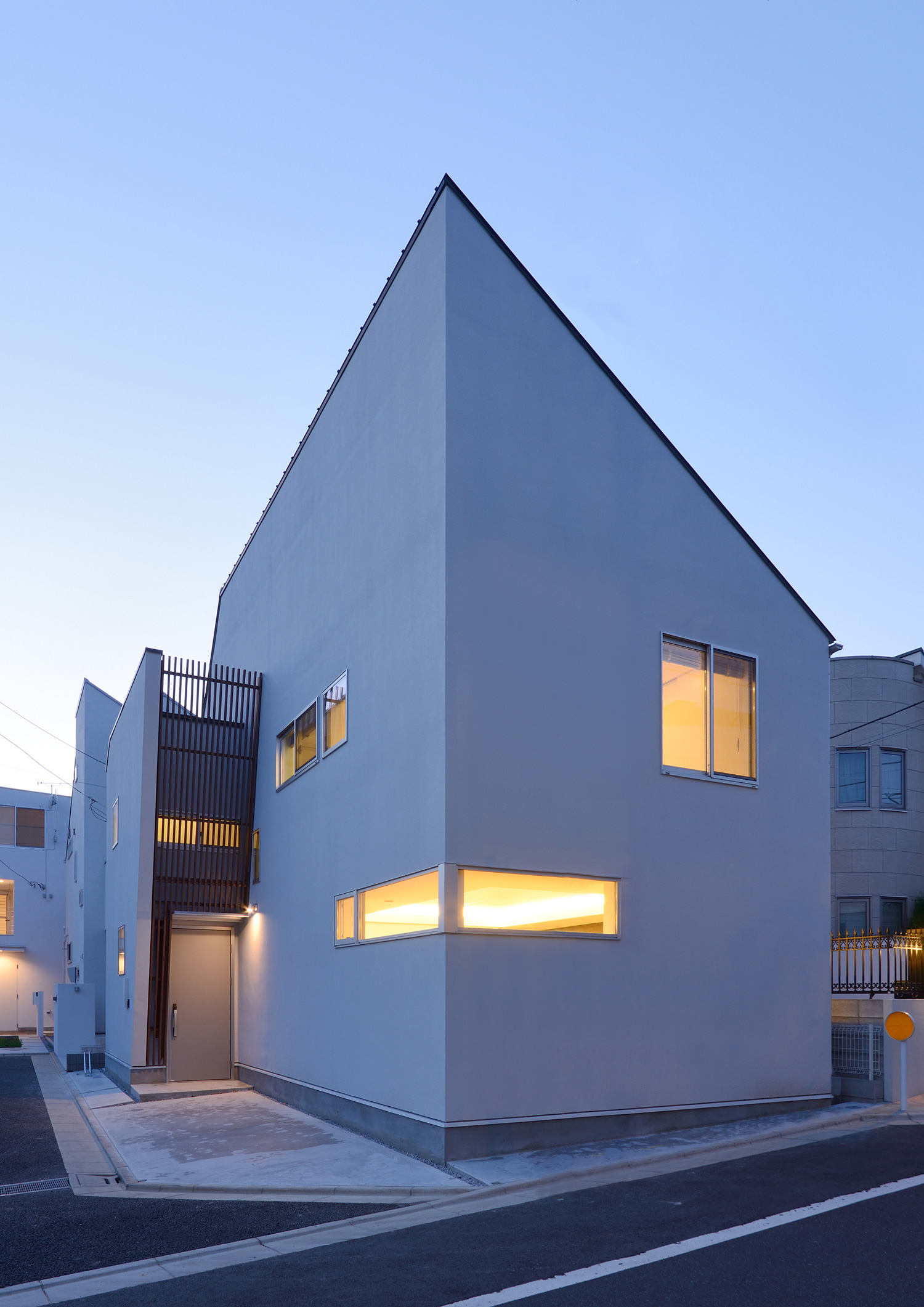 スリット窓から室内の光が漏れる、斜め屋根で白い外壁の住宅・デザイン住宅