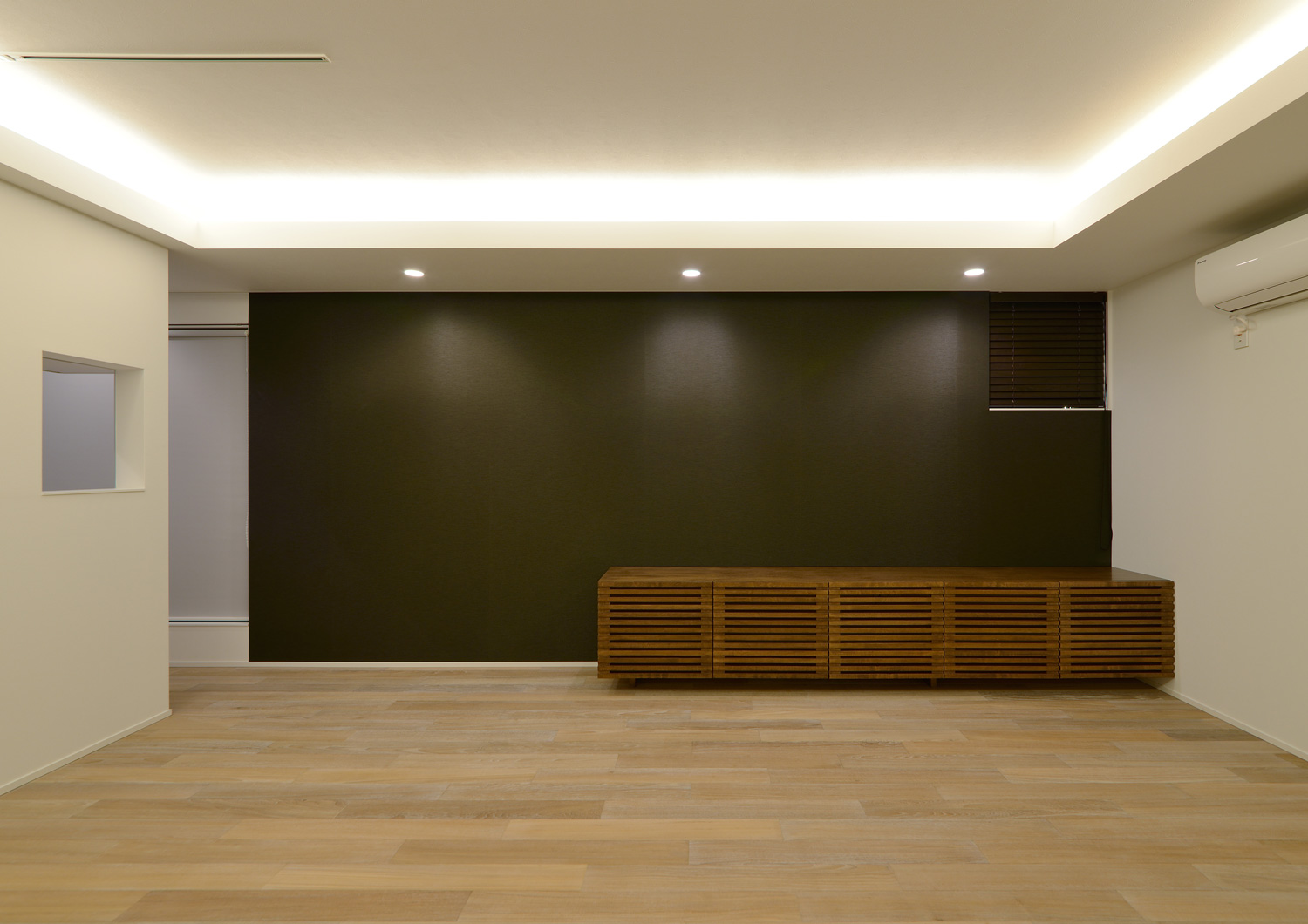 天井の間接照明と、黒い壁の上に取り付けられたダウンライトに照らされるLDK・デザイン住宅