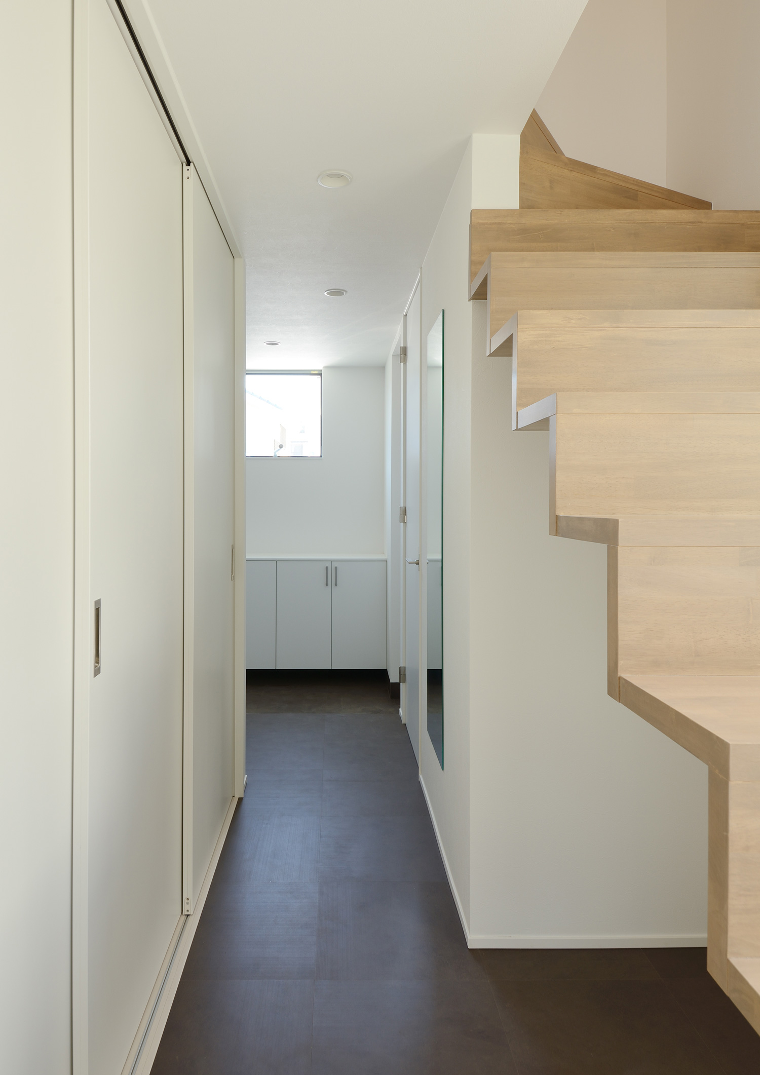 木製の階段のそばにある、ダークブラウンの床で、壁や建具が白の廊下・デザイン住宅