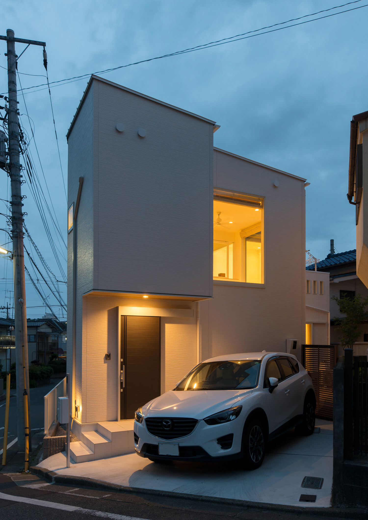 白い車が一台止められた、白い外壁で黒い玄関扉が取り付けられた家・デザイン住宅