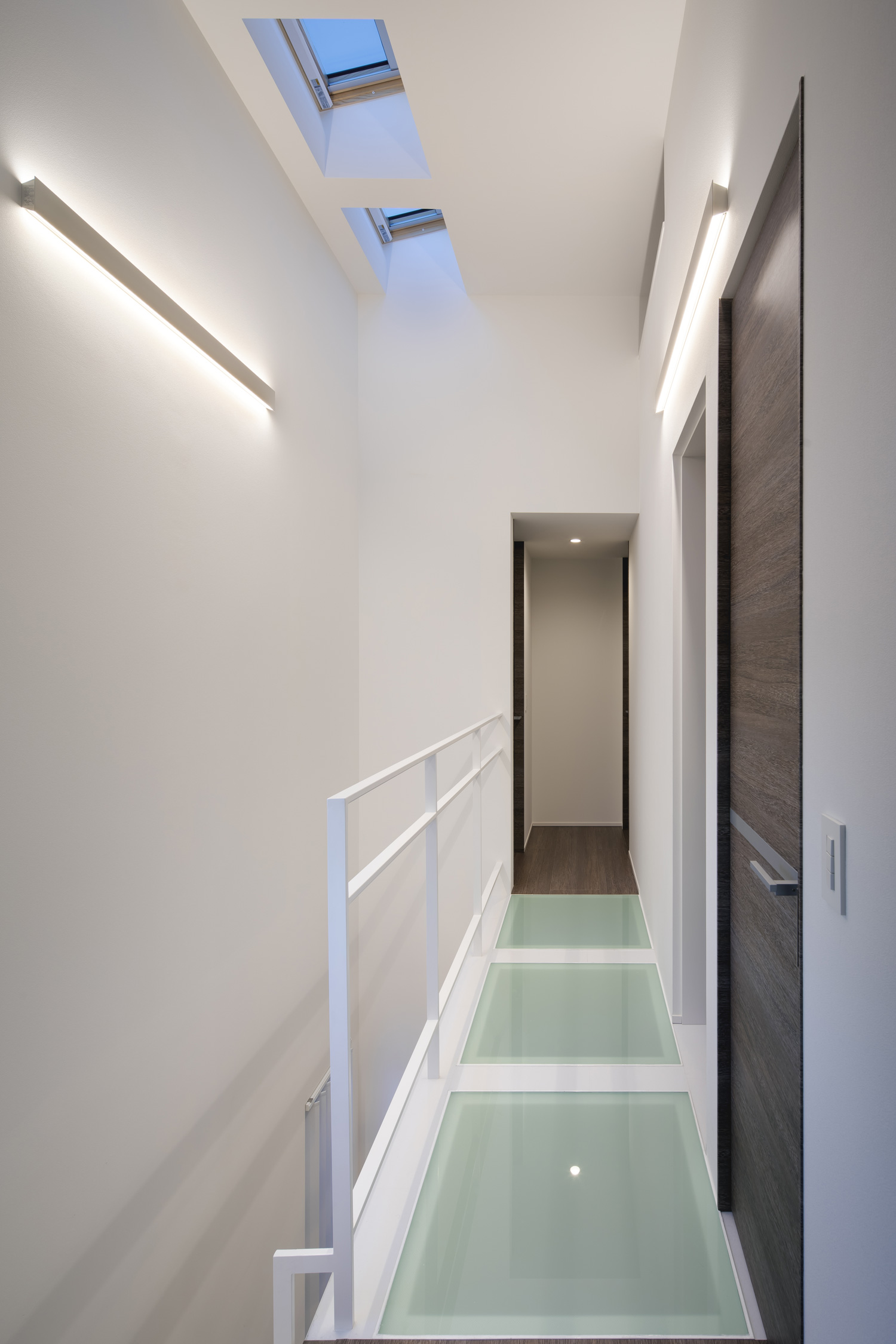 壁に間接照明を取り付けたガラス床の廊下・デザイン住宅