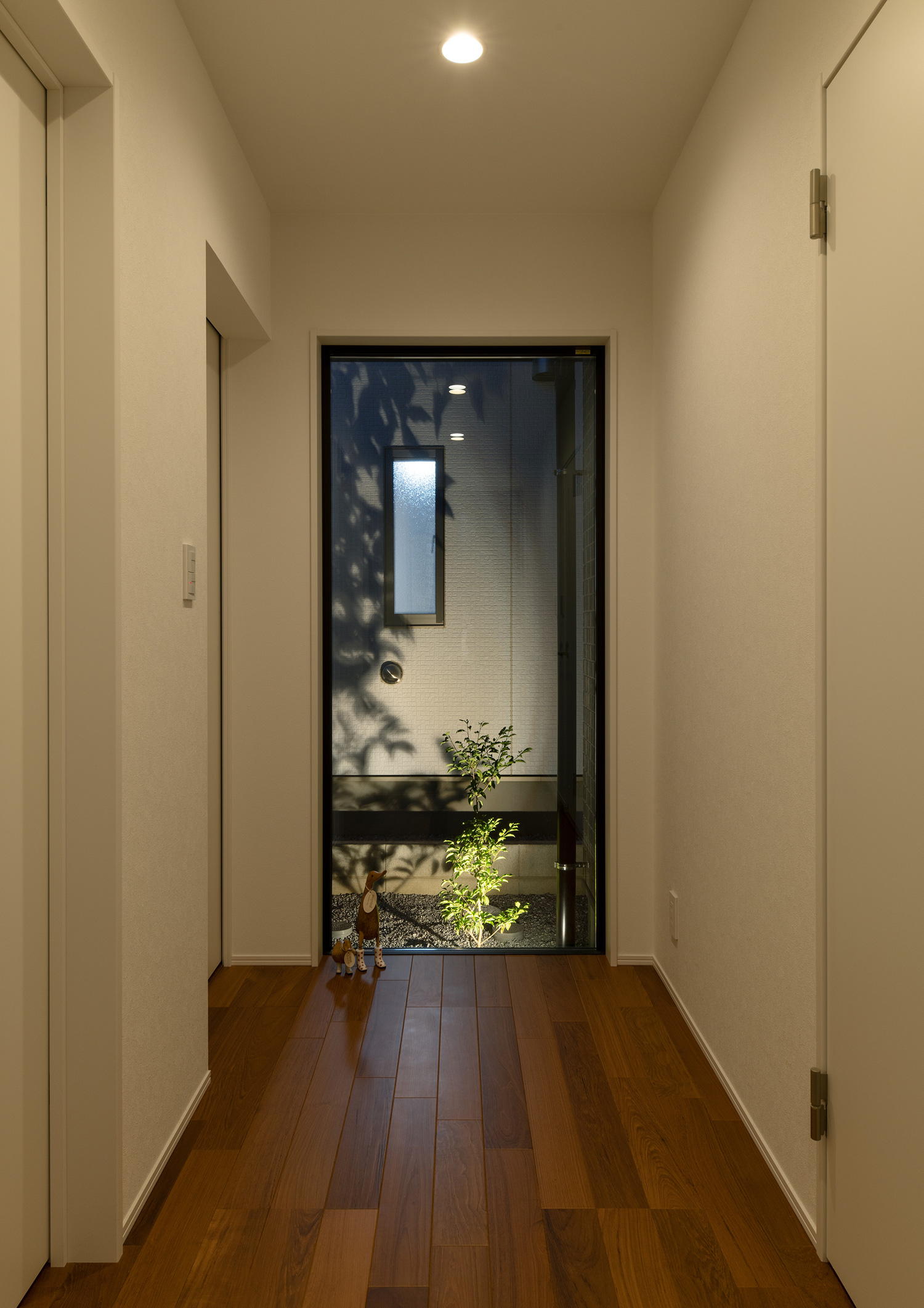ライトアップされた植栽が見える、廊下の突き当りにあるFIX窓・デザイン住宅