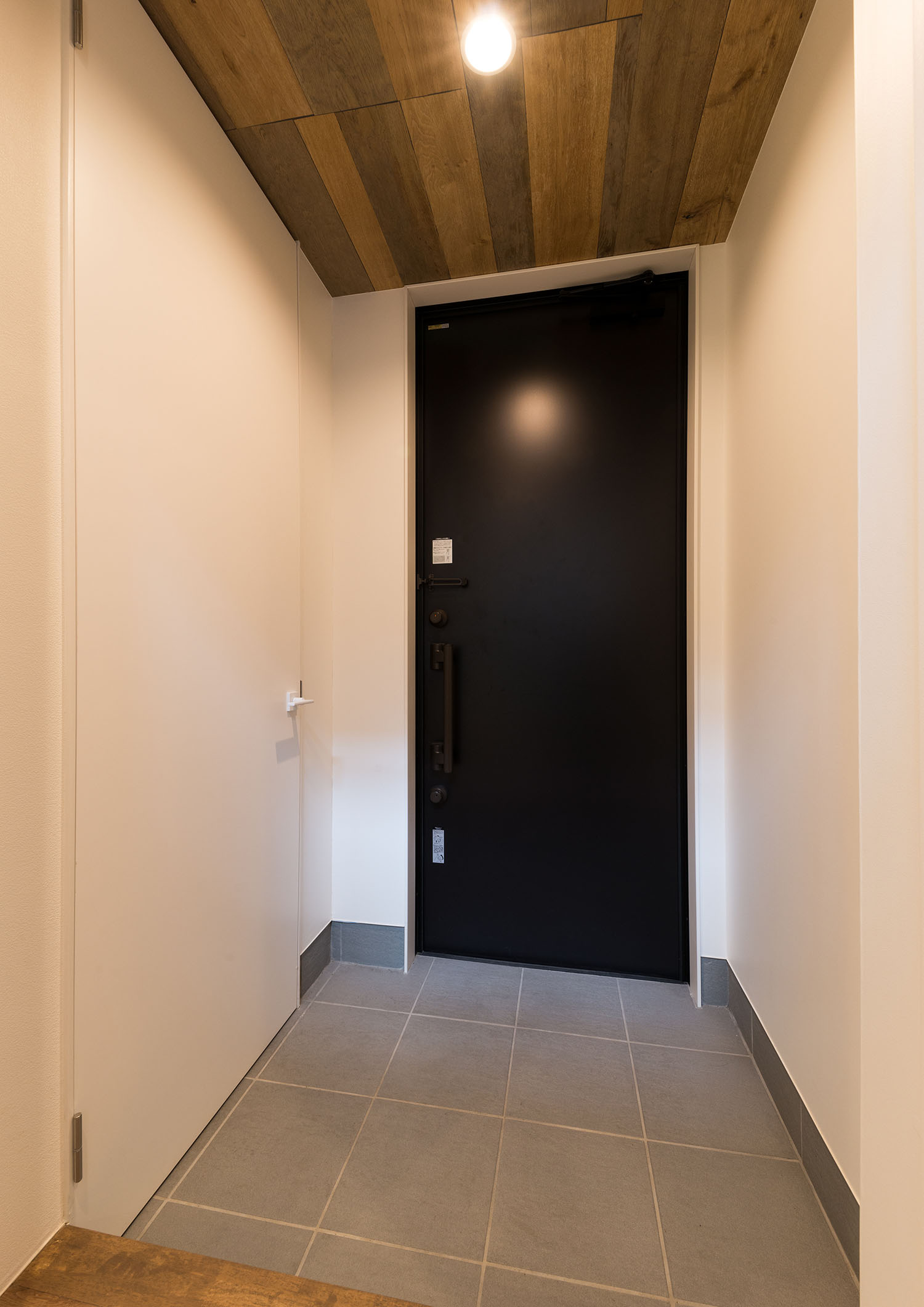 木目の天井とタイルの床で、扉が黒い玄関・デザイン住宅