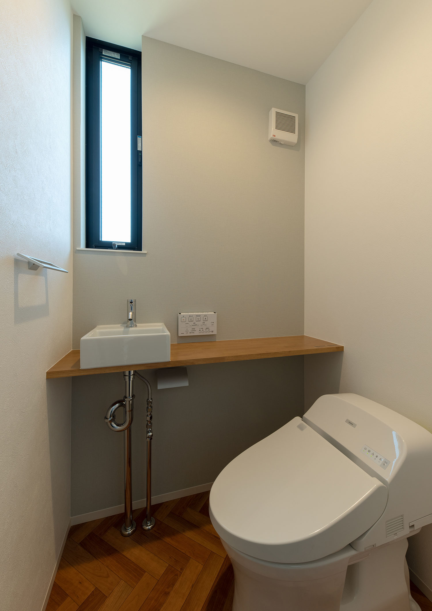スリット窓と薄型手洗いがあるヘリンボーン柄の床のトイレ・デザイン住宅