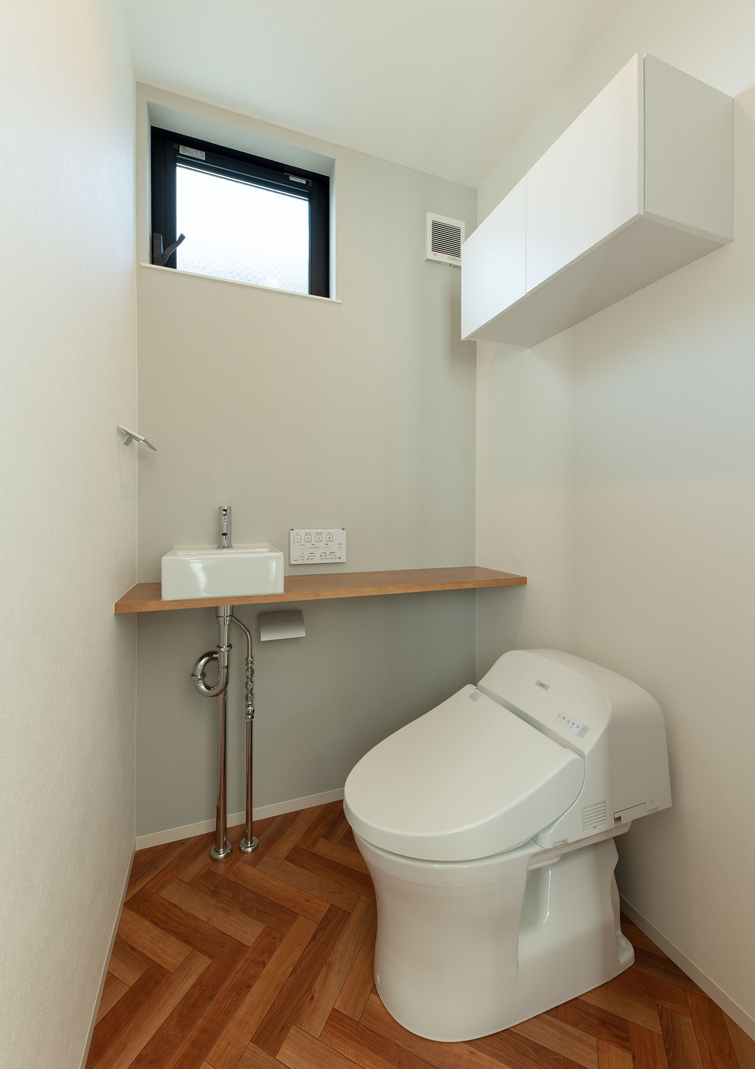 薄型手洗いと収納があるヘリンボーン柄の床のトイレ・デザイン住宅