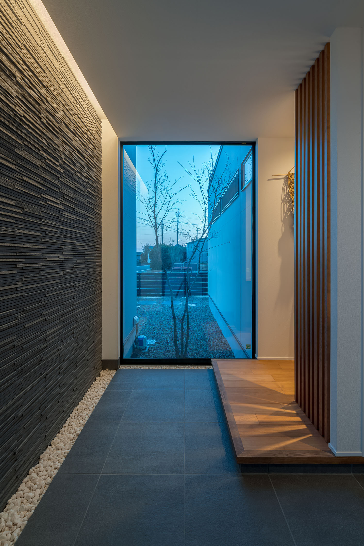 石の壁を照らすように間接照明が取り付けられた玄関・デザイン住宅