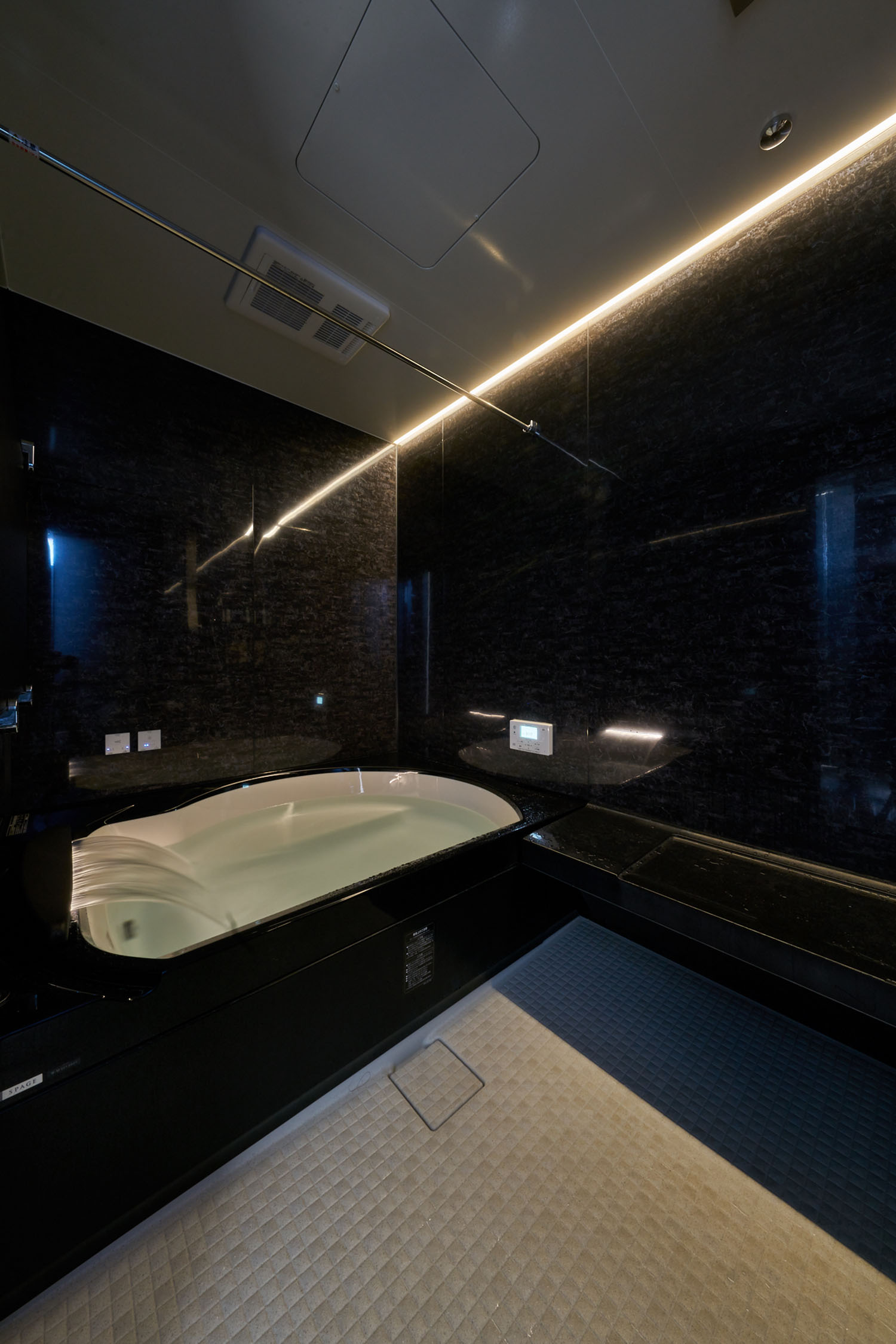 壁に間接照明が取り付けられた黒を基調とした浴室・デザイン住宅