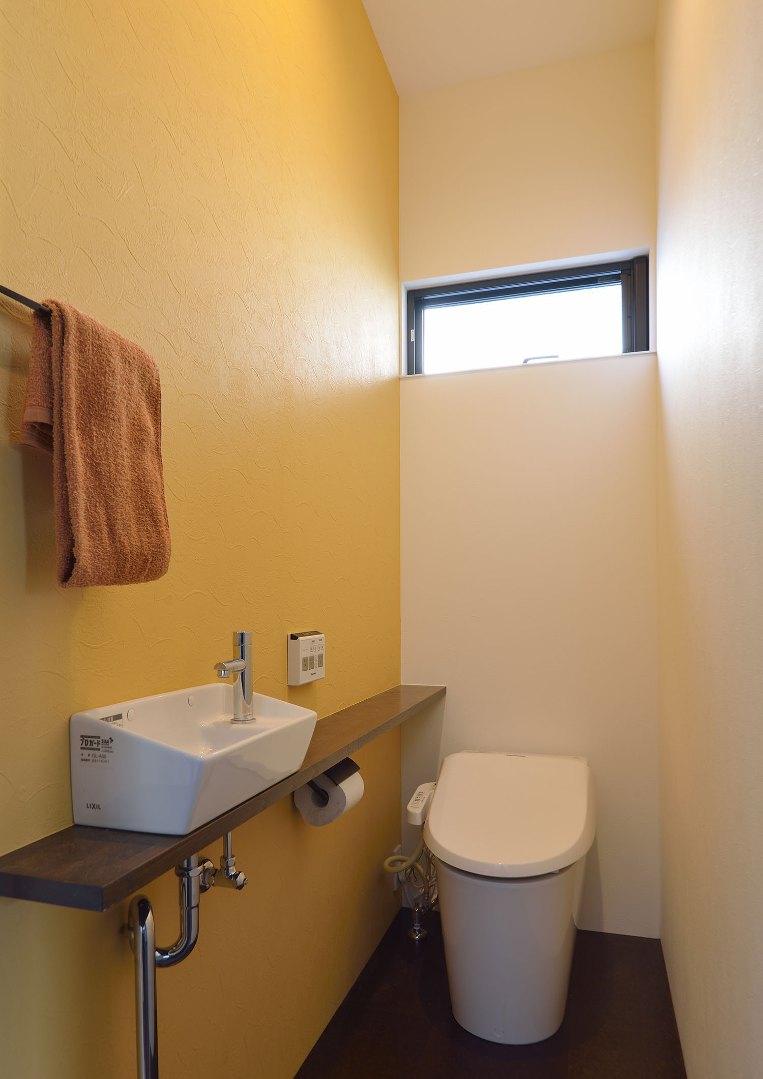 スリット窓や手洗いカウンターがある、黄色のアクセントクロスのトイレ・デザイン住宅