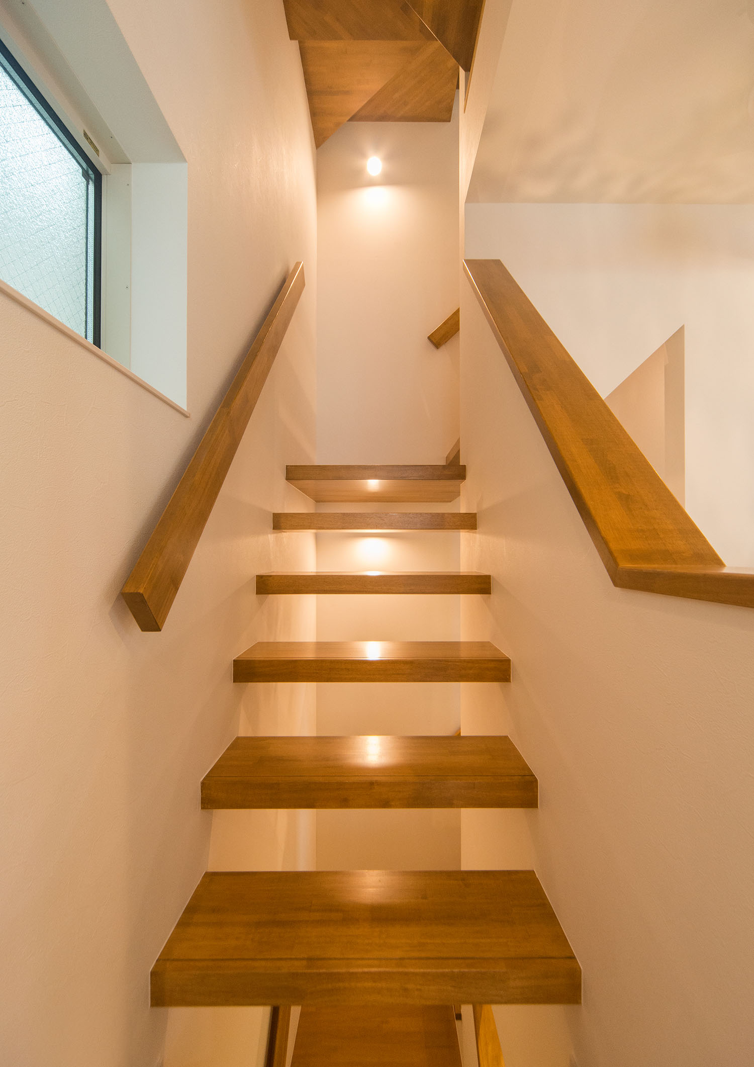 スポットライトに照らされる、壁付の木のスケルトン階段・デザイン住宅