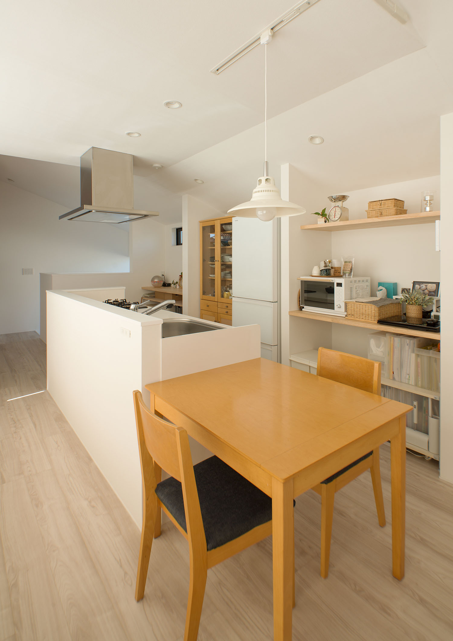 白い腰壁付きのアイランドキッチンの横に並べられる形で置かれた、二人掛けの木のダイニングテーブル・デザイン住宅