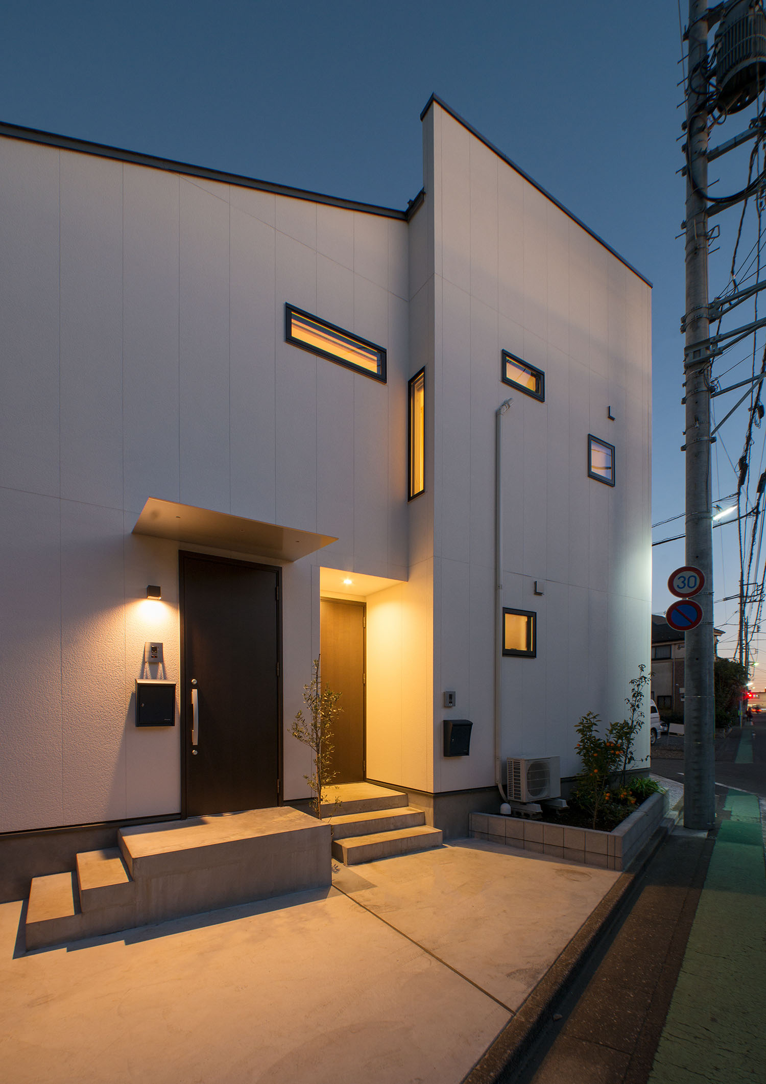 扉の色が違う二つの玄関が、それぞれ照明で照らされている様子・デザイン住宅