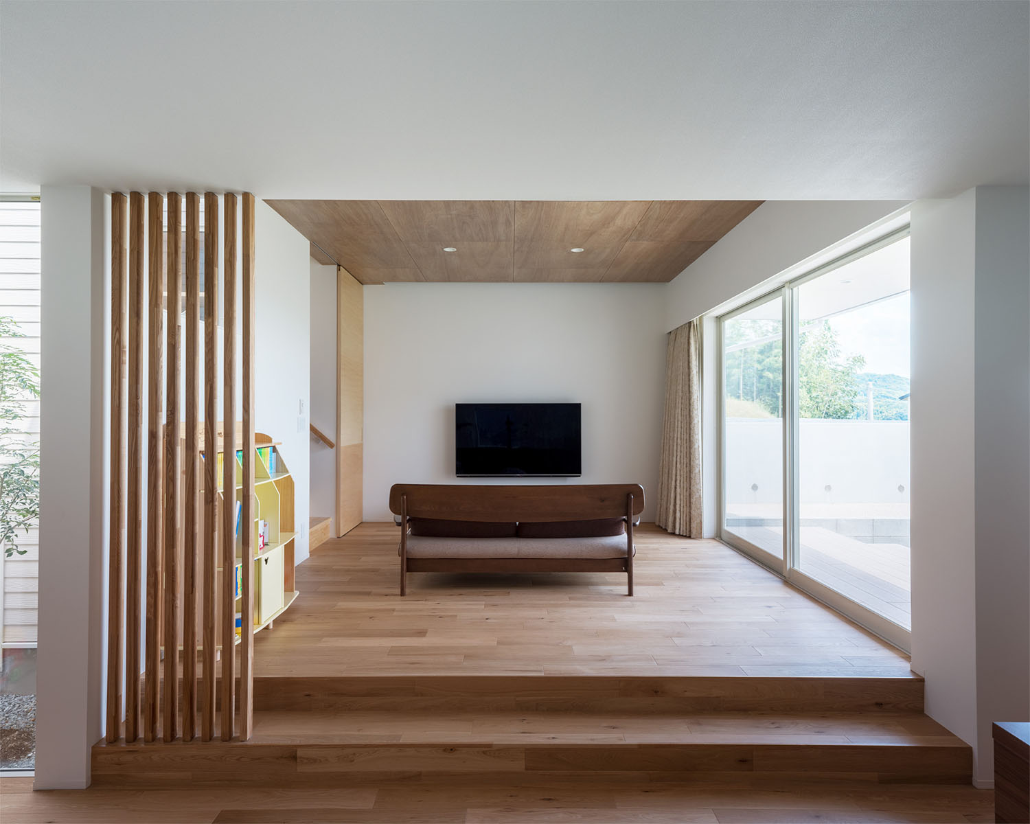 大きな窓があり、ソファーとテレビが置かれた木材を中心としたLDK・デザイン住宅