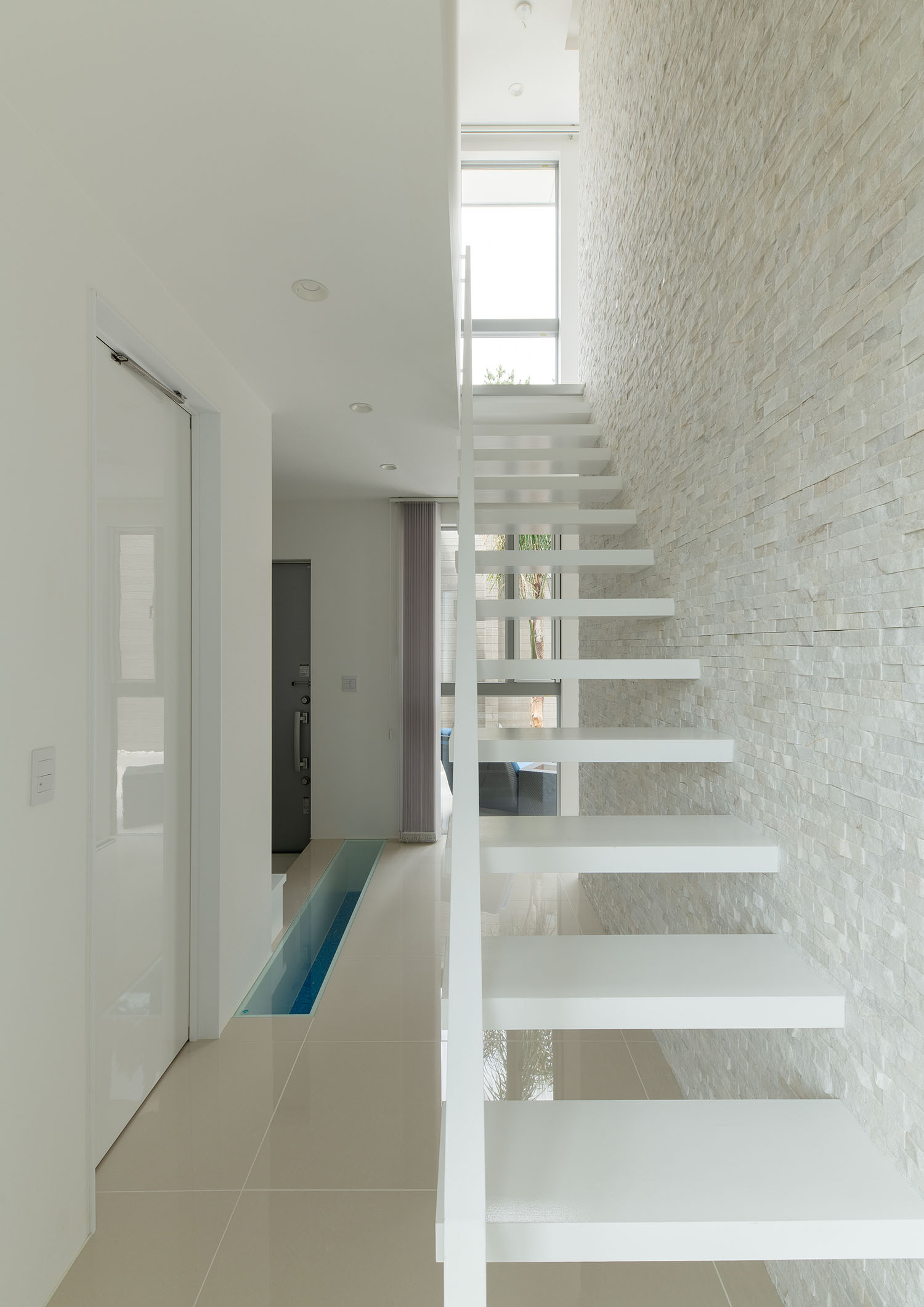 白いタイルの壁に付けられた白いスケルトン階段がある廊下・デザイン住宅