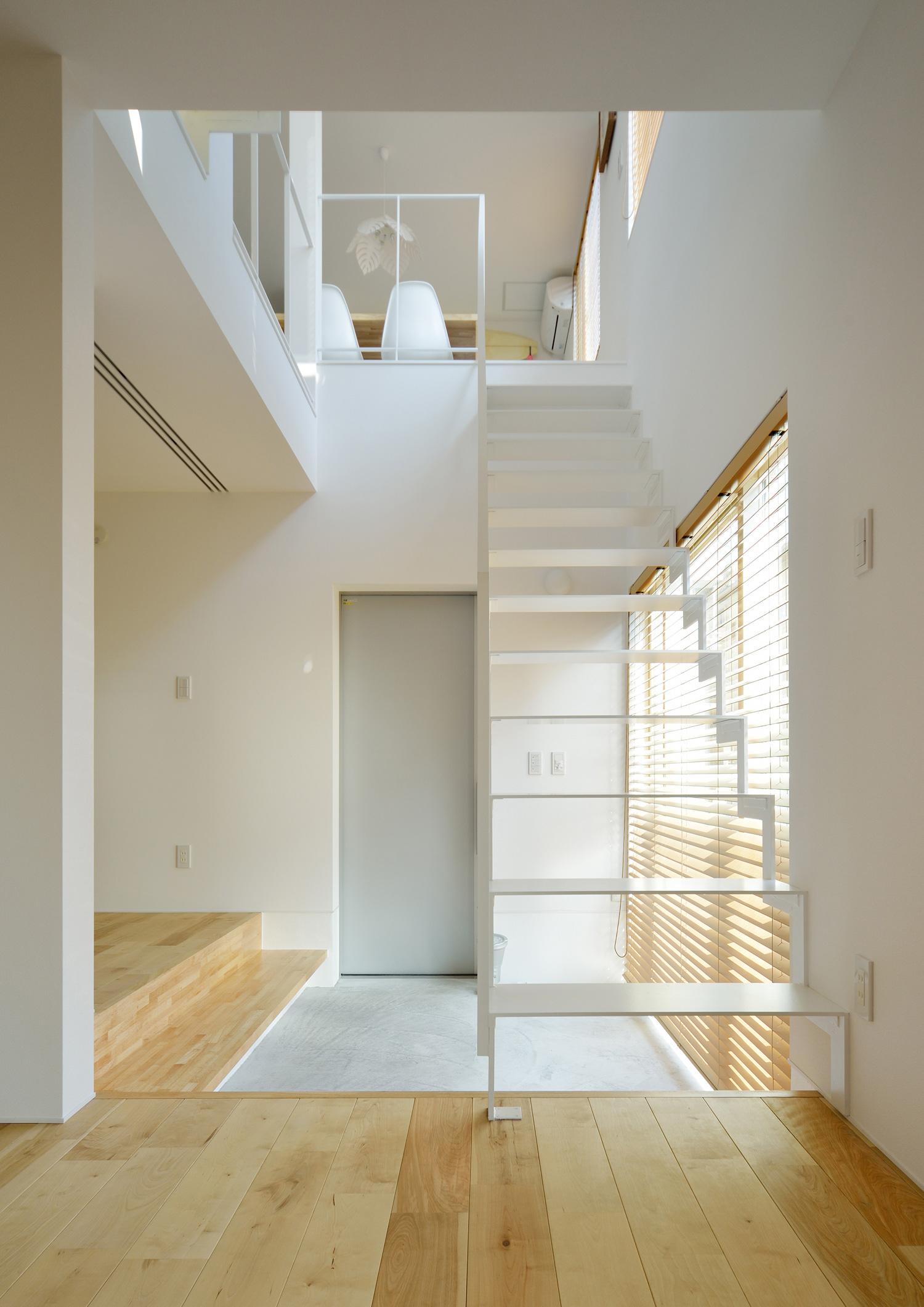 土間玄関の上を横切る白い金属製のスケルトン階段・デザイン住宅