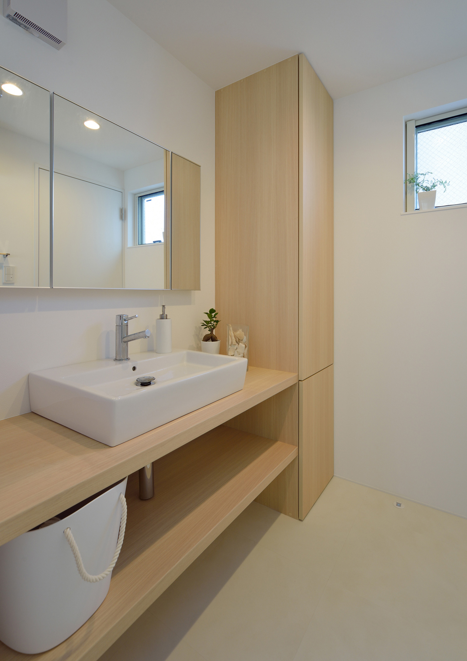 木の造作洗面台や木の扉付き収納ボックスがある明るい洗面所・デザイン住宅