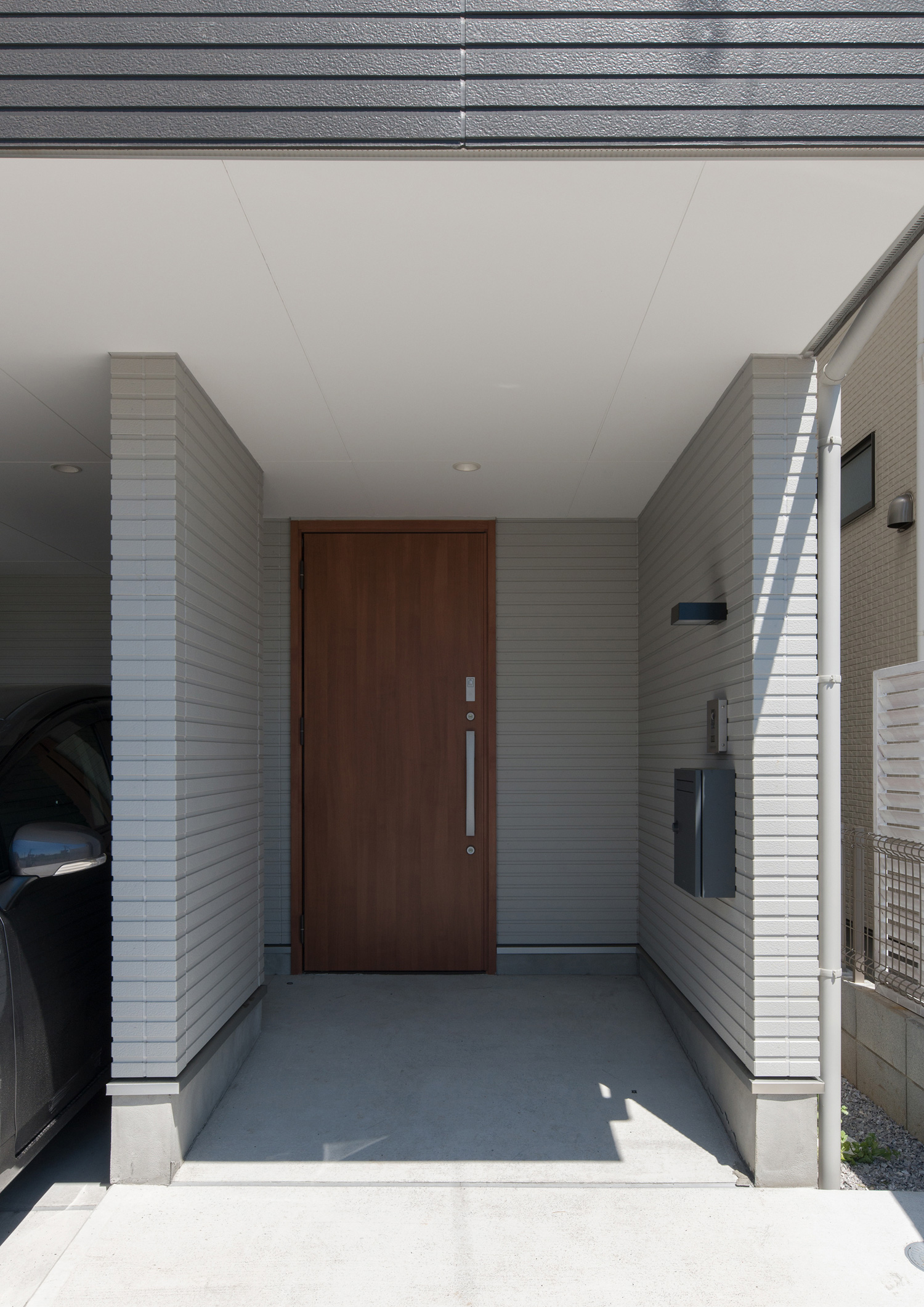白い壁に木目の玄関扉が取り付けられた玄関ポーチ・デザイン住宅