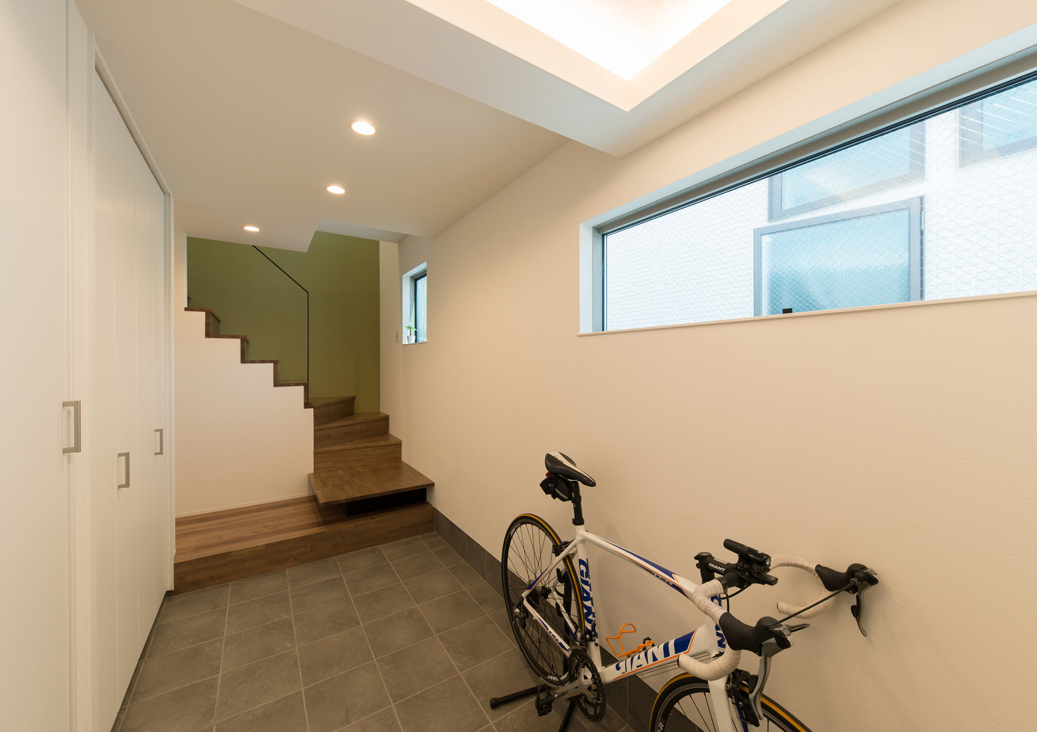 自転車を置くスペースがあるシンプルなタイルの玄関・デザイン住宅