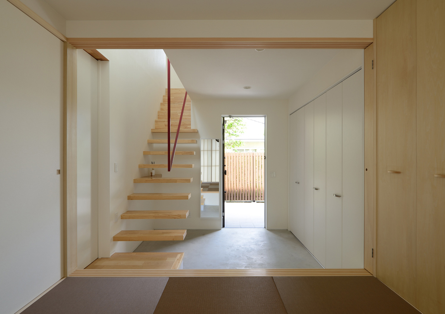 和室から、スケルトン階段が横切るモルタルの広い玄関を見た様子・デザイン住宅