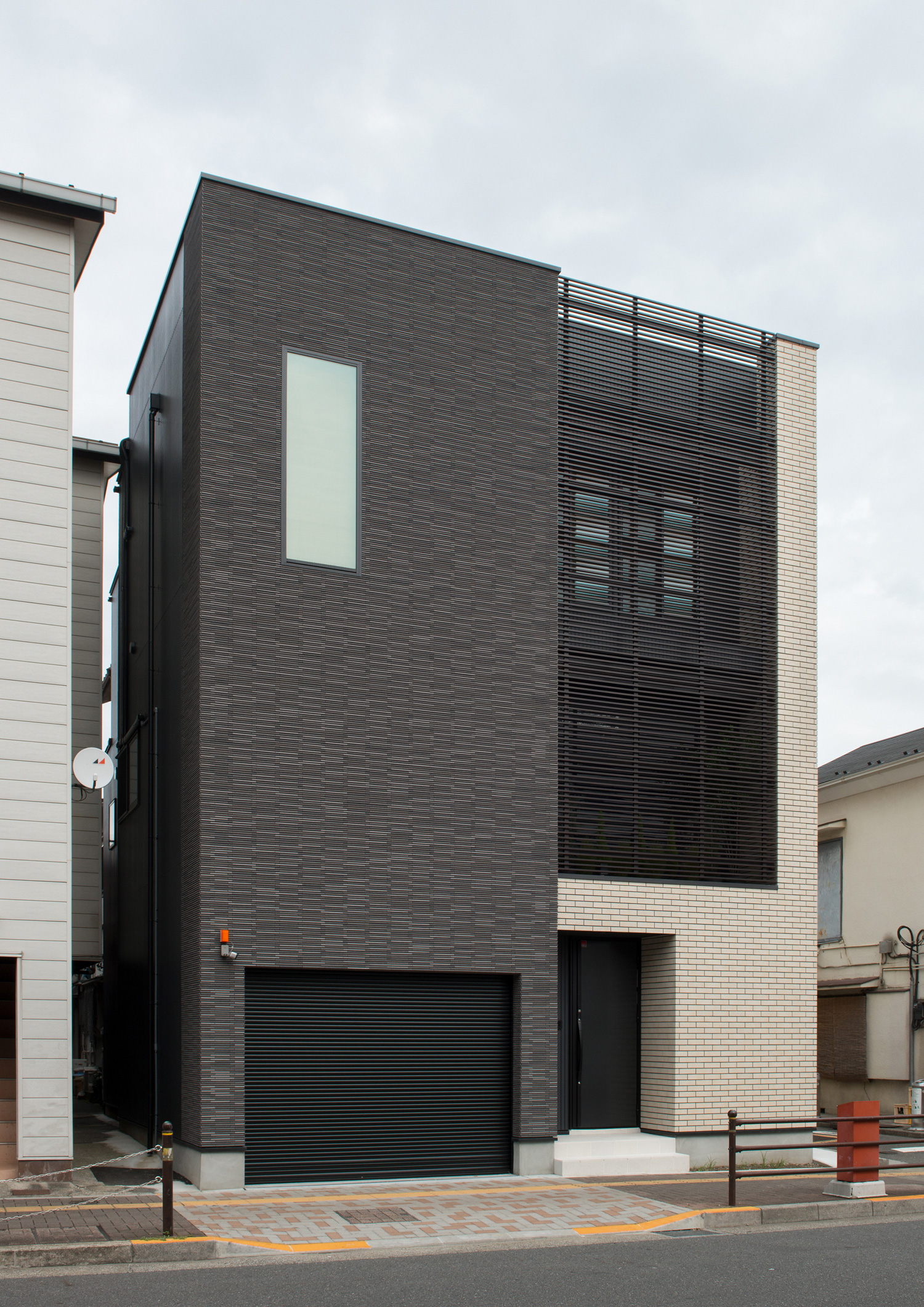 白と黒の二種類のタイルの外壁でルーバーの目隠しがある外観・デザイン住宅