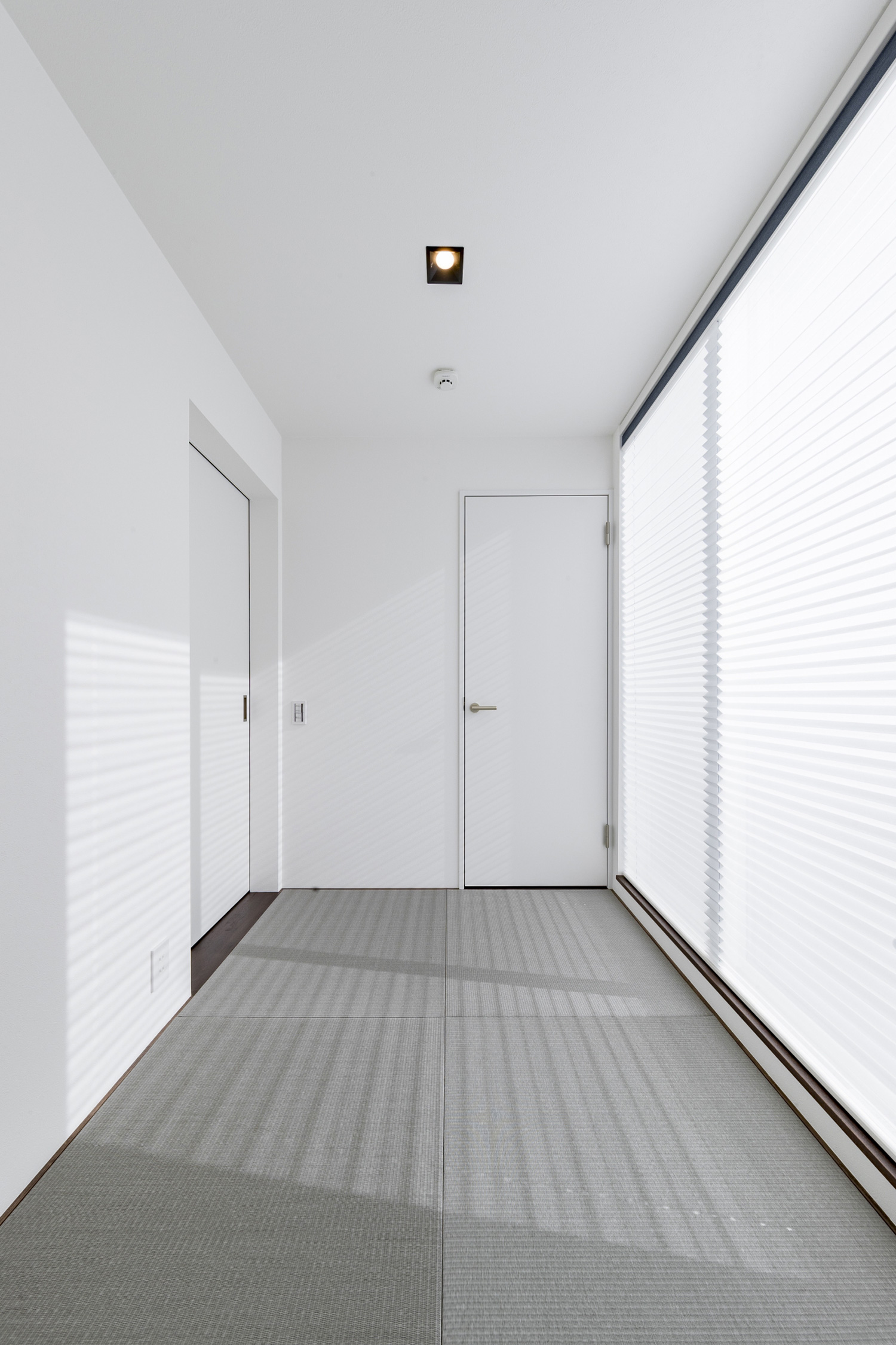 グレーの琉球畳で、大きな窓がとりつけられた白い壁の和室・デザイン住宅