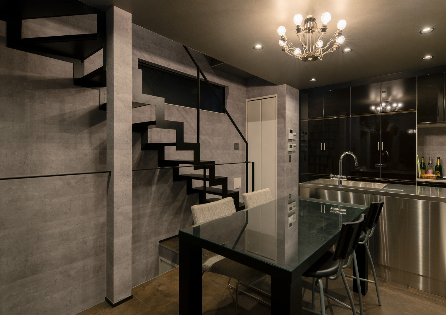 シャンデリアに照らされるアイアンのスケルトン階段やステンレスのカウンターキッチンがあるLDK・デザイン住宅