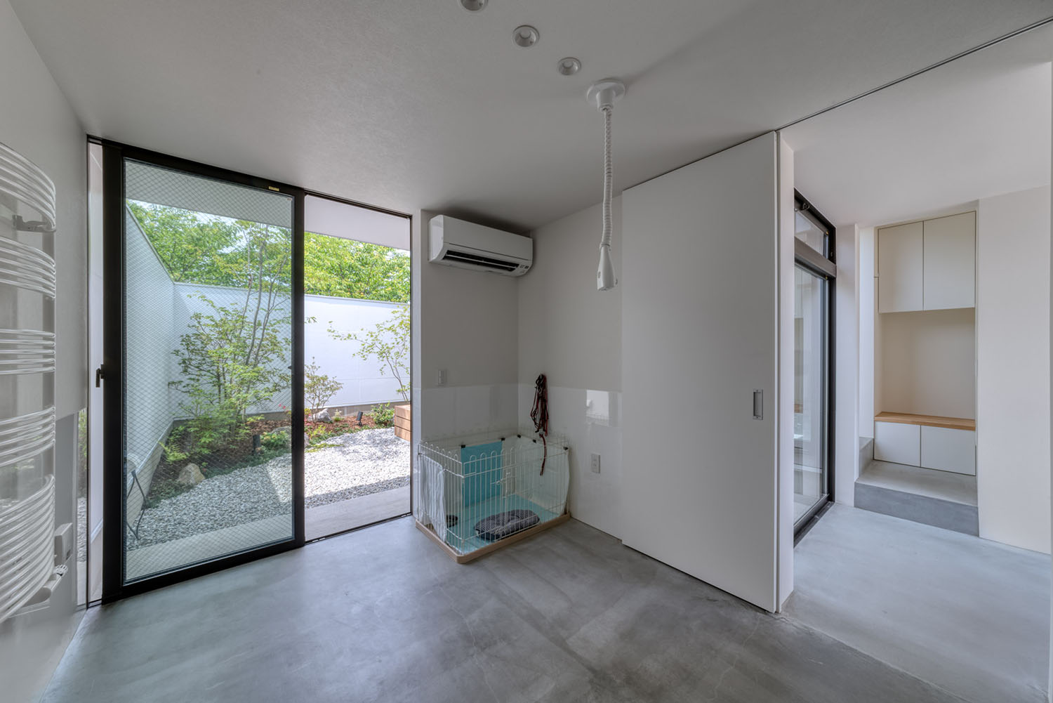 白を基調としたモルタルの床の空間にケージが置かれている様子・デザイン住宅