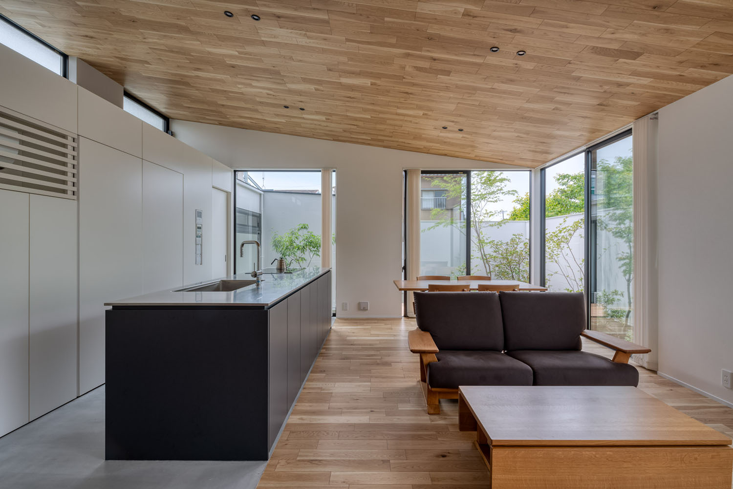 天井や床に木材を使用した空間に黒いアイランドキッチンがある様子・デザイン住宅