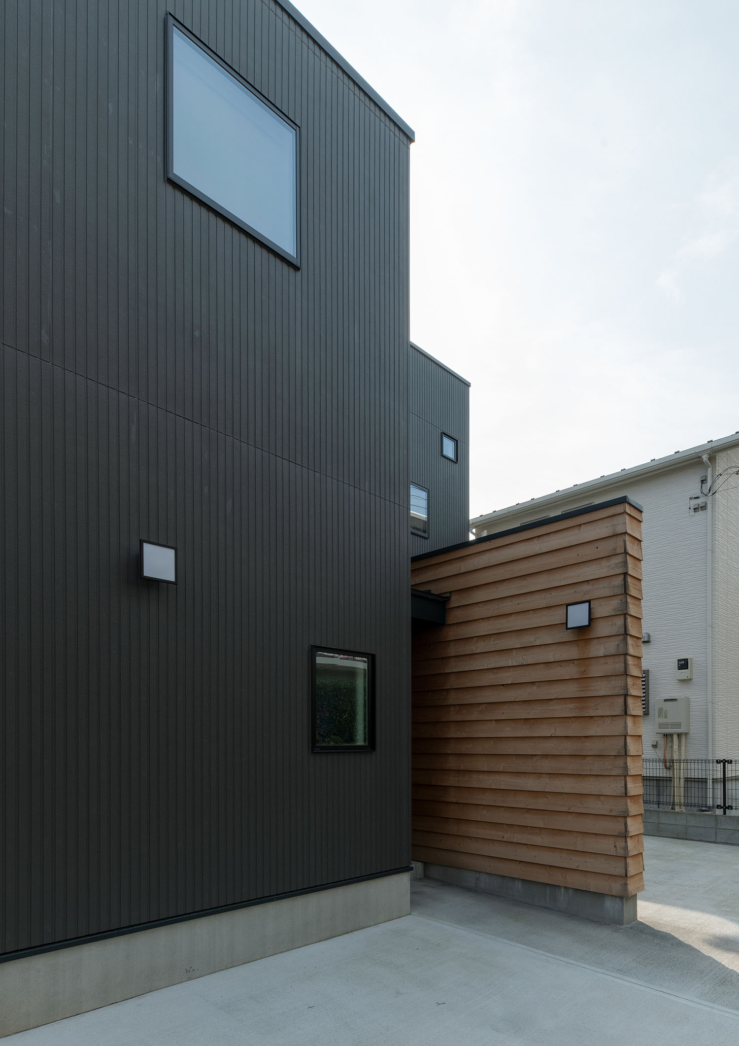 黒を基調とした外観に木材を使用した壁が建てられている住宅・デザイン住宅