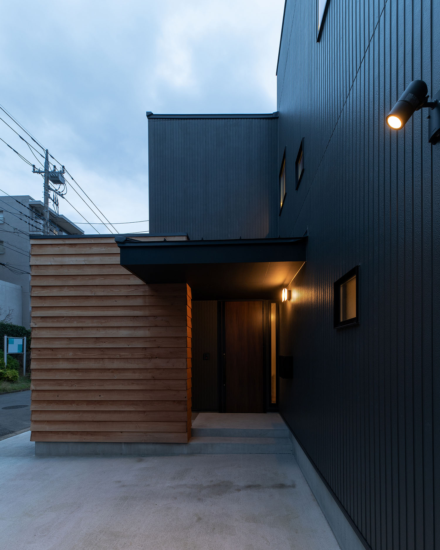 木材の壁が立てられた黒い外壁の住宅に屋外照明が取り付けられている・デザイン住宅