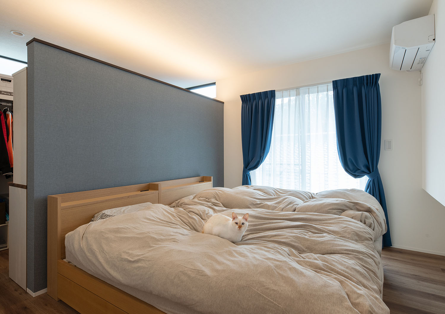 ベッドの他に青いカーテンや青い壁が設けられている寝室・デザイン住宅