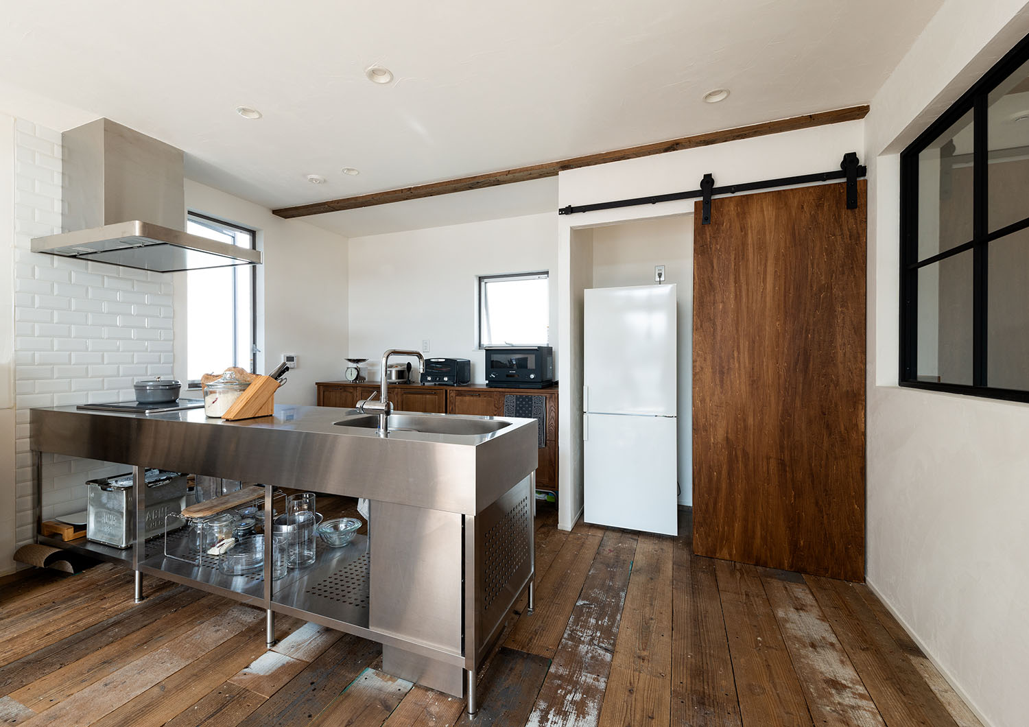 ステンレスのペニンシュラキッチンが木材を多く使用した空間にある・デザイン住宅